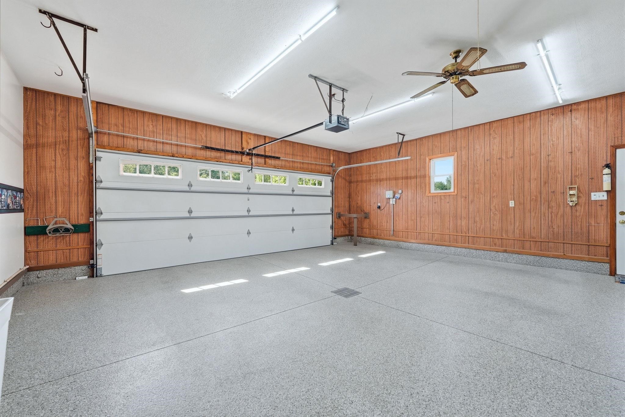 Spacious garage featuring wood-paneled walls, a single window, and a white overhead garage door with integrated windows