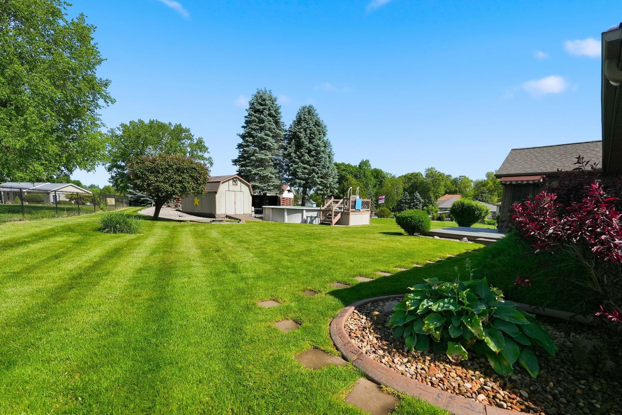 Expansive green lawn with mature trees and a dedicated garden bed