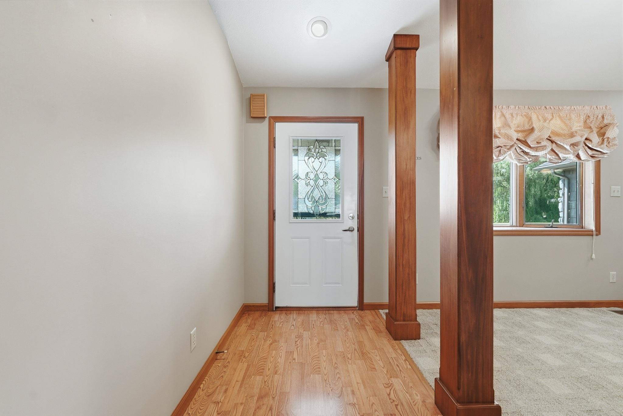 Entryway featuring wood-finish flooring, a white door with decorative glass inserts, and two substantial wood-clad structural columns