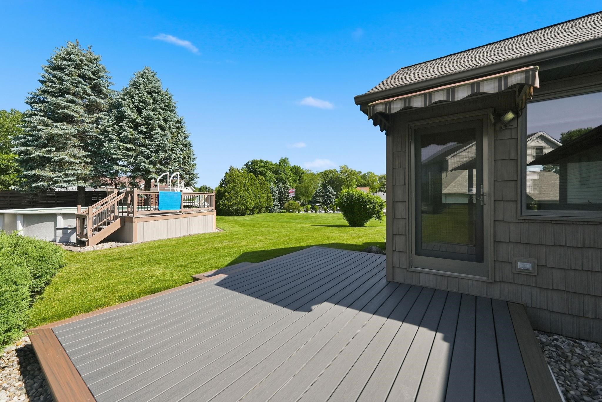 Expansive backyard featuring a composite deck, an above-ground pool with a surrounding wood deck, a manicured lawn, and mature trees