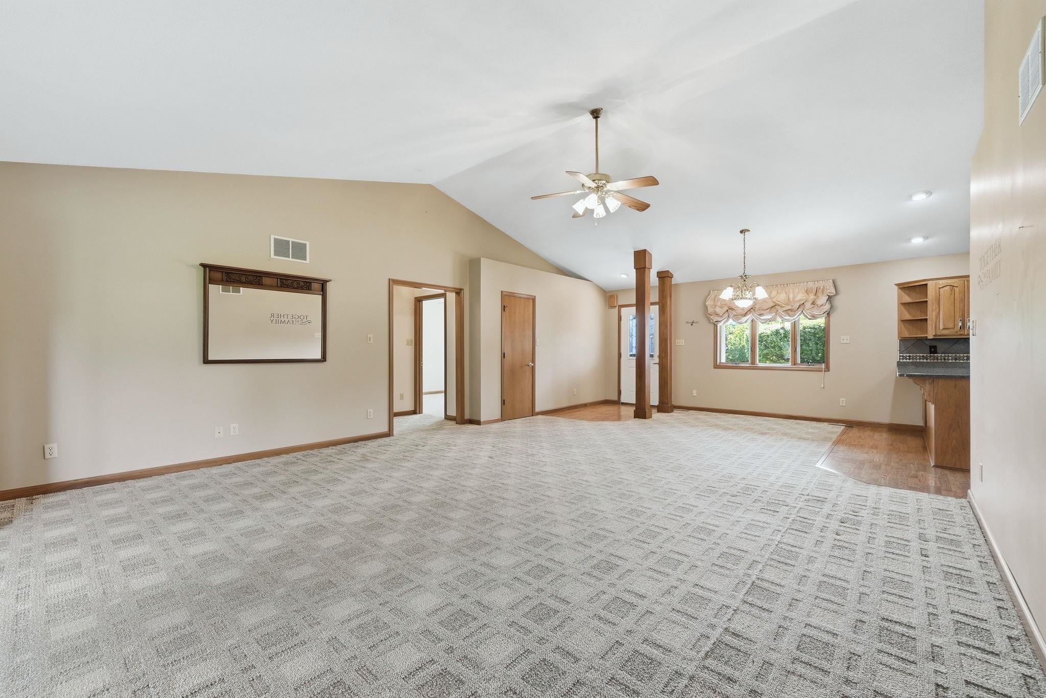 Spacious room featuring vaulted ceilings, patterned carpet flooring, a ceiling fan, and decorative support pillars