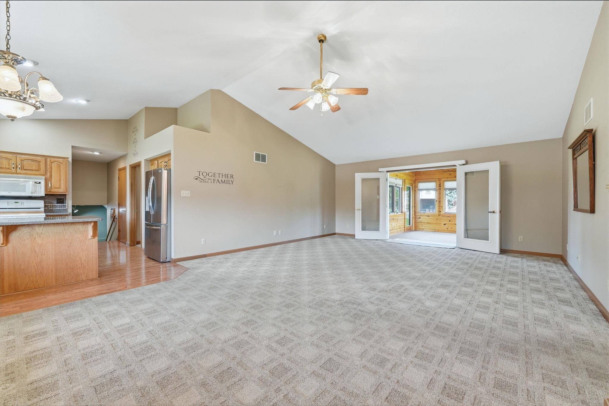 Spacious living area featuring vaulted ceilings, a ceiling fan, and patterned carpet flooring