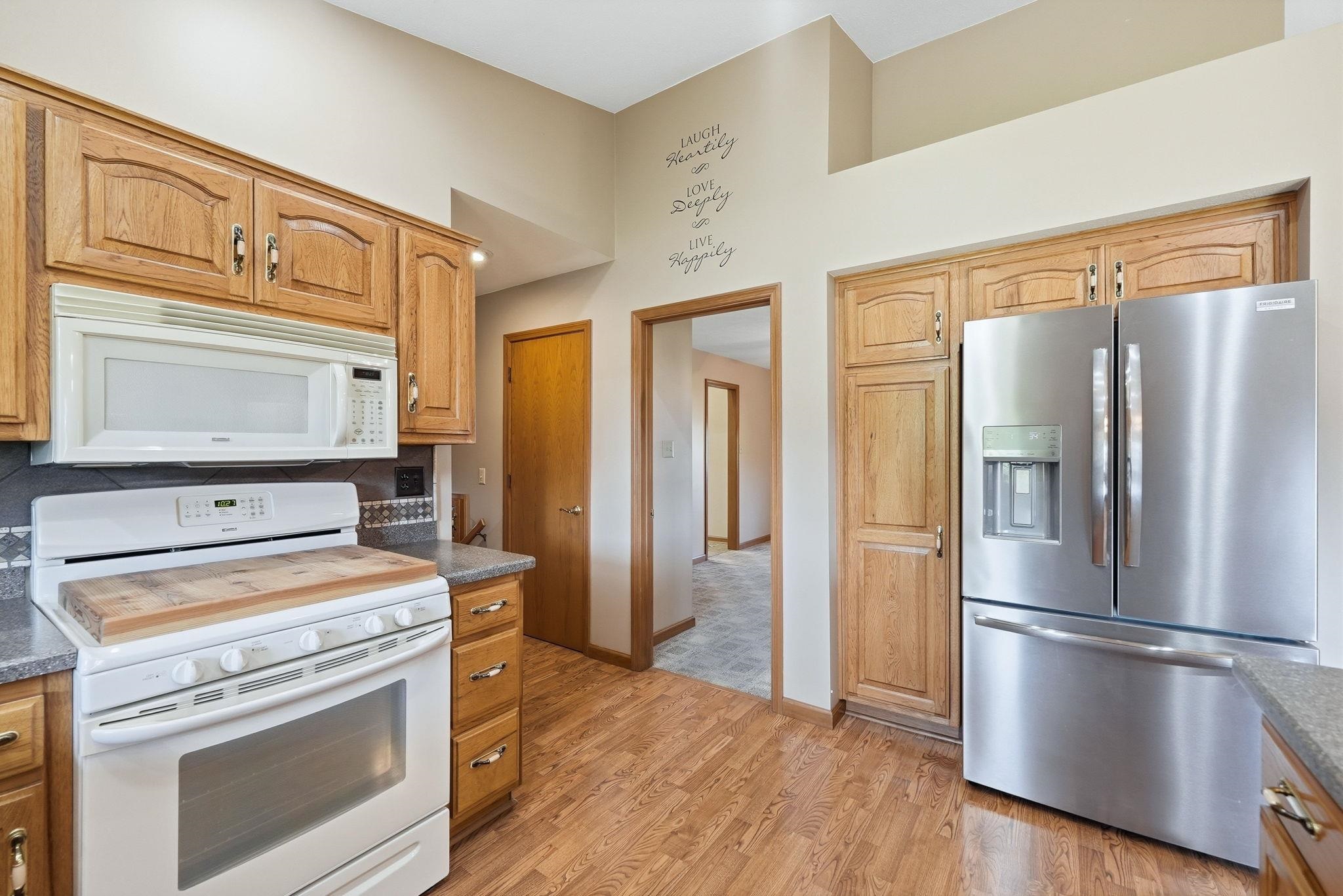 Kitchen featuring wood-finish flooring, natural wood cabinetry, light-toned countertops, white overhead microwave, and stainless steel French door refrigerator