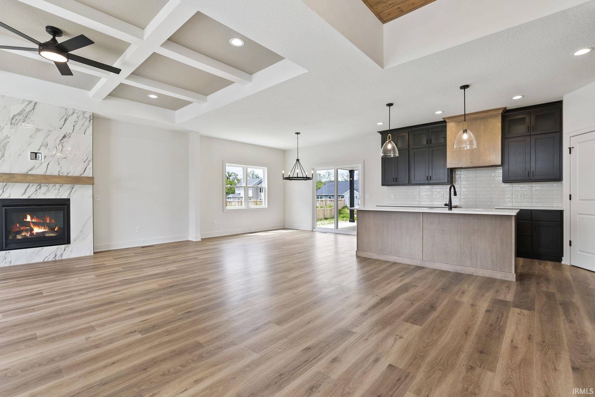Open-concept living area featuring wood-finish flooring, a contemporary fireplace with a marble-style surround, and an elegant coffered ceiling