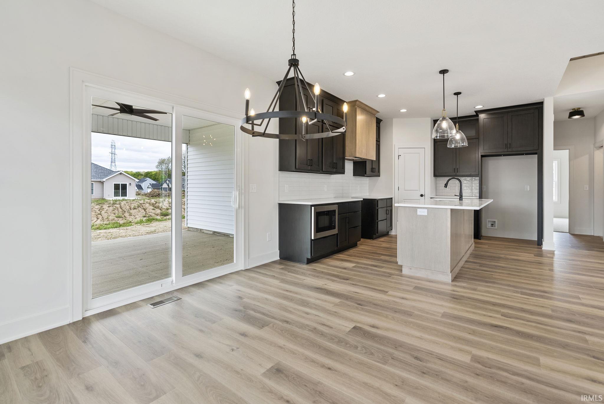 Open-concept kitchen and dining area featuring wood-finish flooring, a kitchen island with seating, dark cabinetry, and white subway tile backsplash