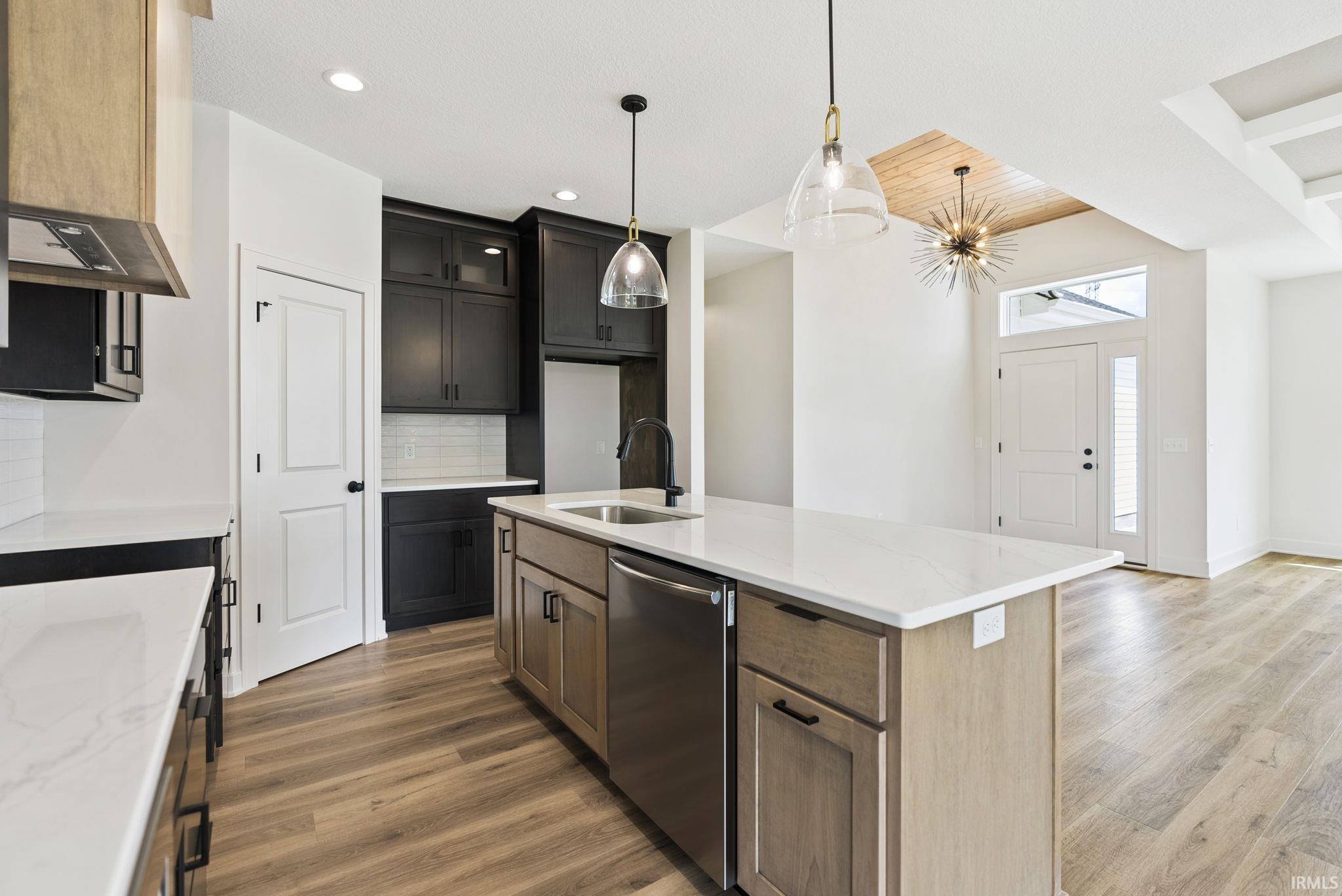 Modern kitchen featuring an island with a stainless steel dishwasher, white countertops, and wood-finish flooring
