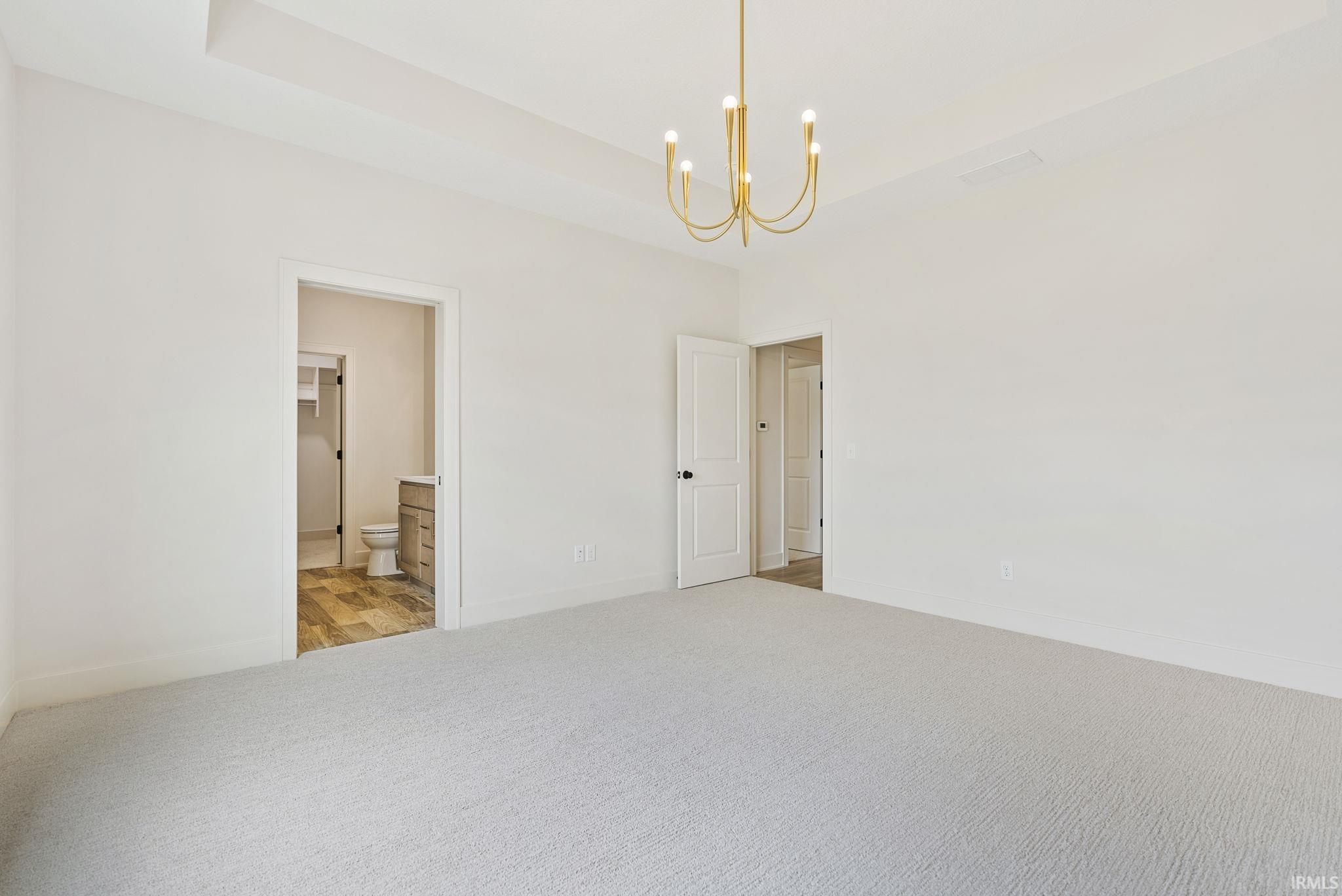 Spacious interior room featuring light-colored carpeting, a tray ceiling, and a contemporary gold-tone chandelier