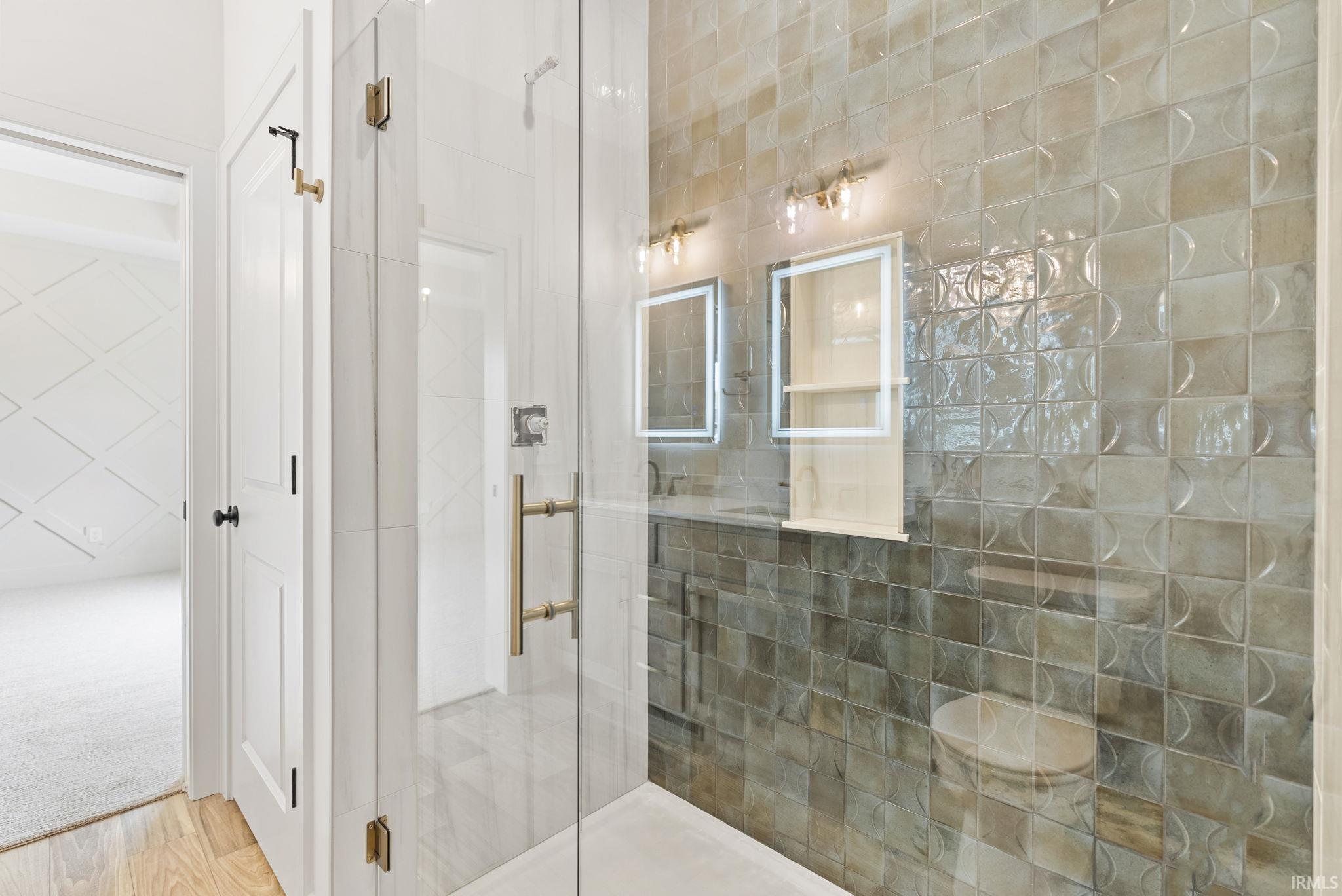 Frameless glass shower enclosure with brass hardware, accented by textured wall tiles and built-in mirrored medicine cabinets