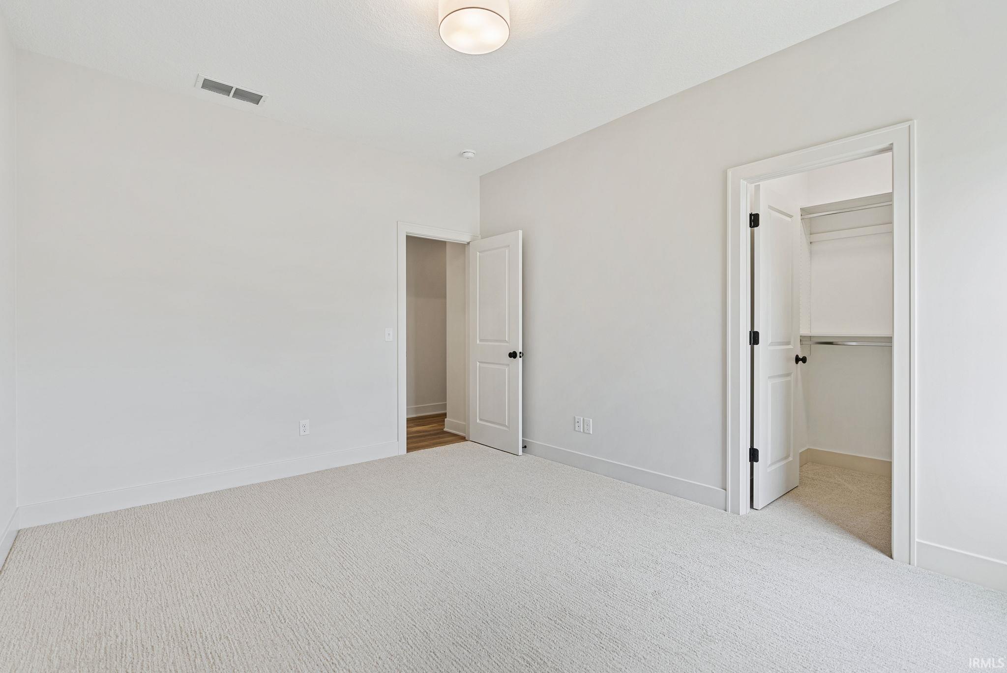 Bright bedroom featuring light-toned carpeting, white walls, and a contemporary ceiling light fixture