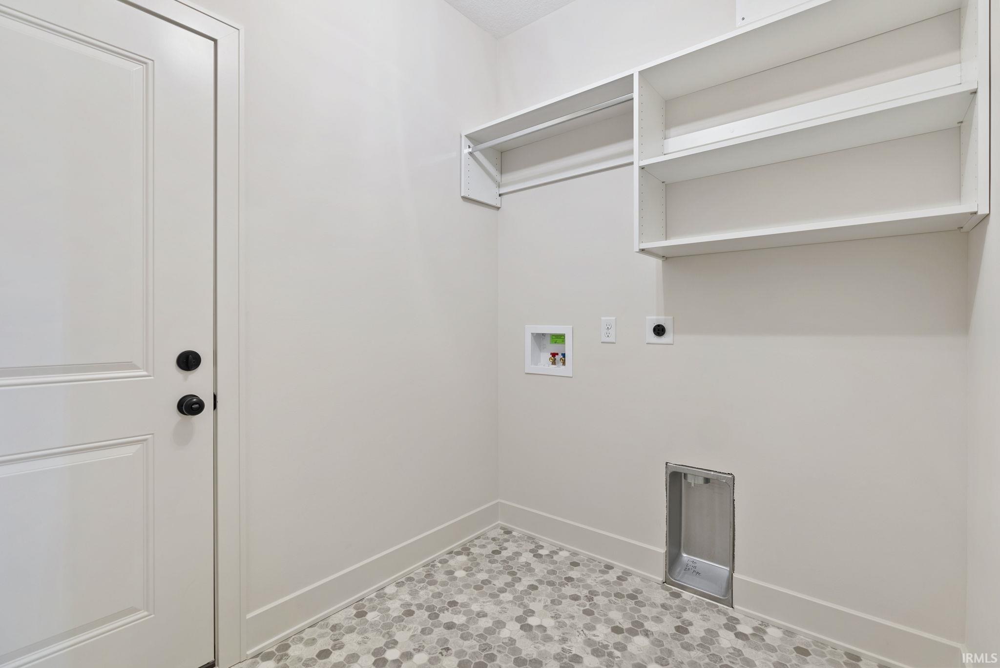 Utility room featuring white shaker-style door with matte black hardware, built-in shelving, hanging rod, and hexagonal mosaic floor tiles