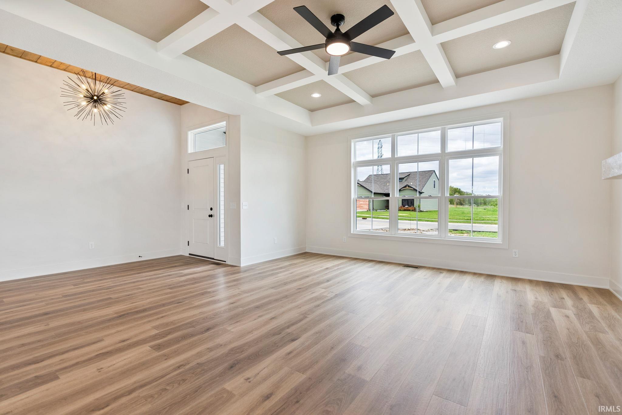 Spacious living area featuring wood-finish flooring, a coffered ceiling with a ceiling fan, and large windows