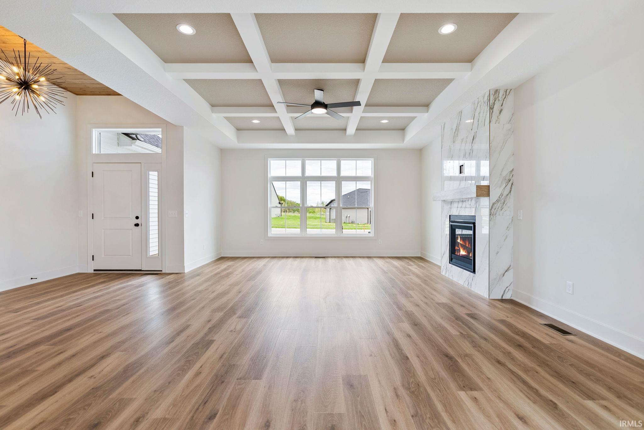 Expansive living area featuring wood-finish flooring, a coffered ceiling with recessed lighting and a ceiling fan, a contemporary fireplace with a stone surround, and large windows