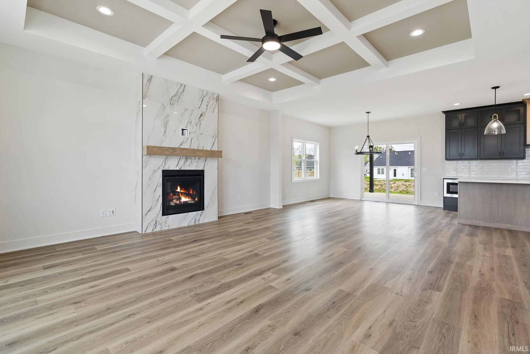 Spacious interior featuring wood-finish flooring, a contemporary fireplace with a marble-style surround and wood mantel, and a coffered ceiling with recessed lighting