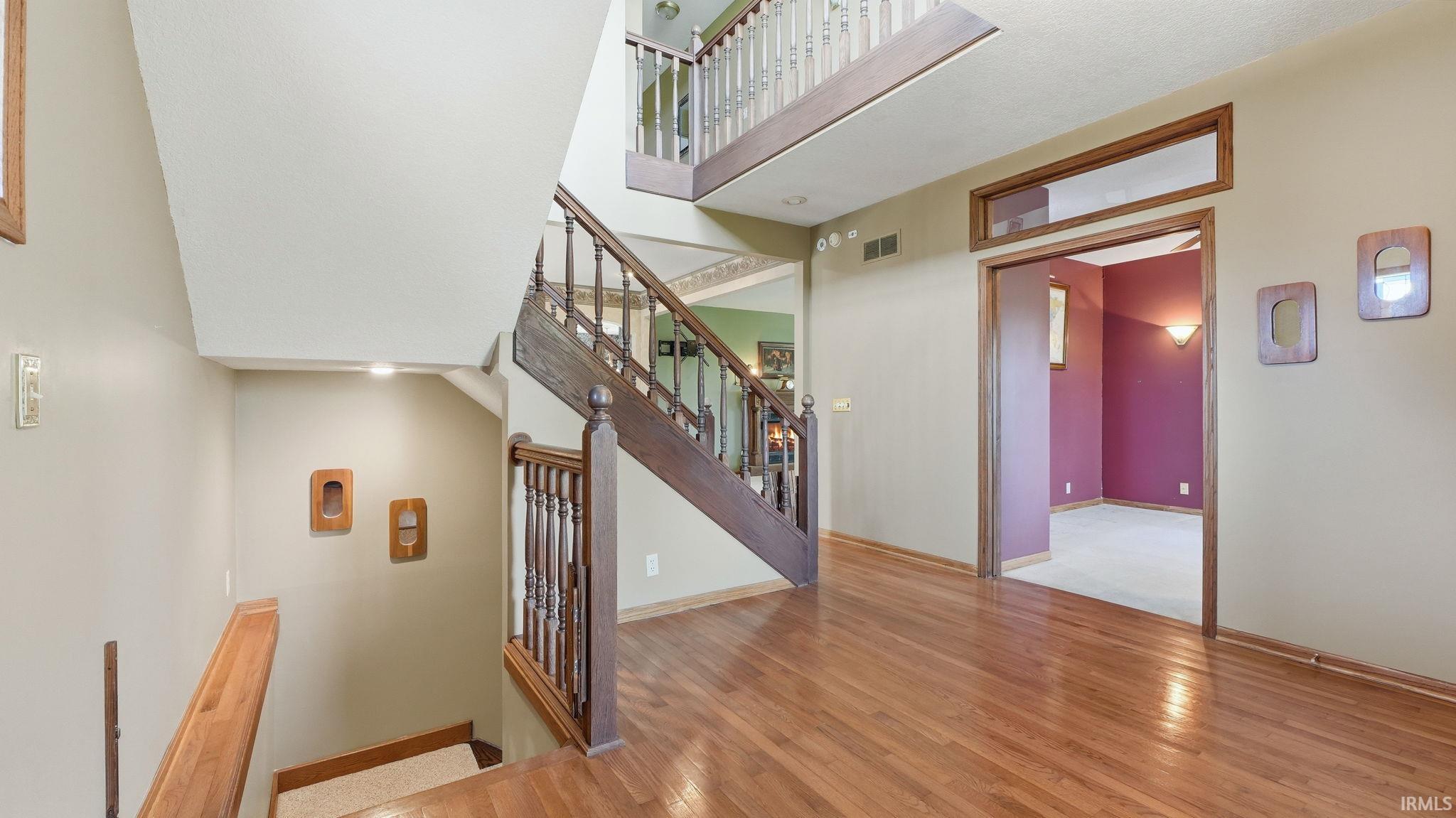 Hardwood flooring featuring an open staircase with wood balusters and handrails, complemented by an upper-level overlook