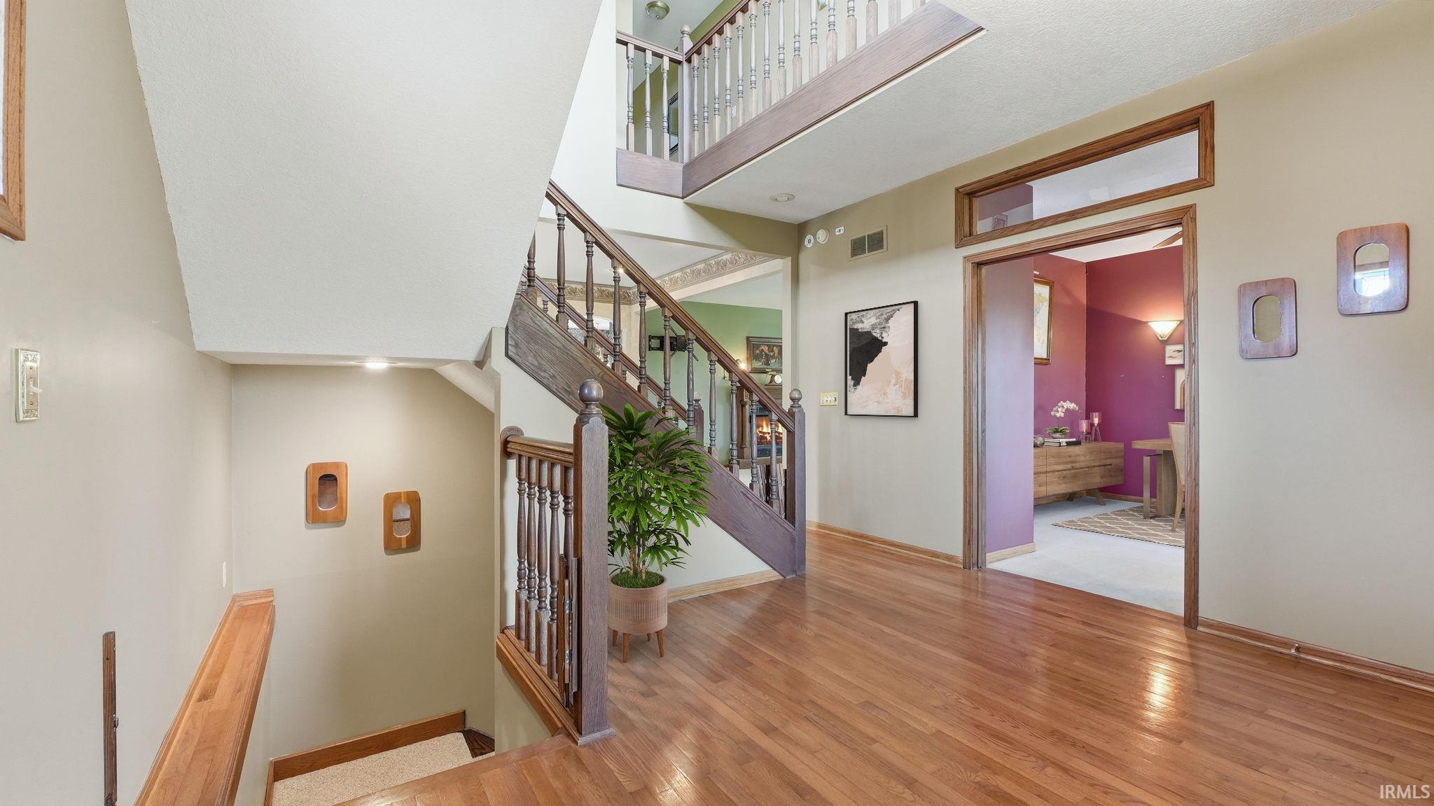 Multi-level interior featuring rich wood-finish flooring, a grand staircase with dark wood newel posts and railings, and a two-story entryway