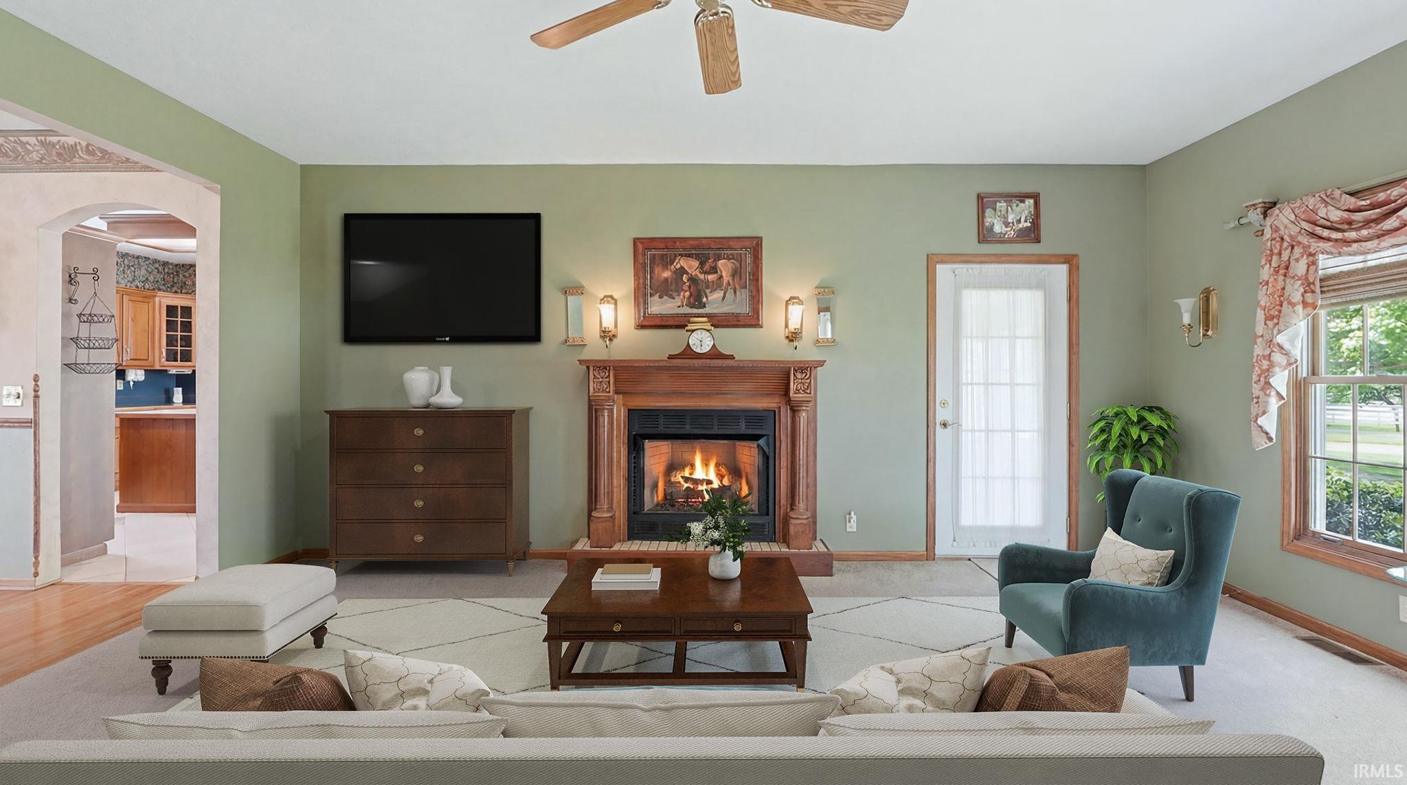 Living room featuring a wood-surround fireplace with hearth, ceiling fan, and a light-colored carpet