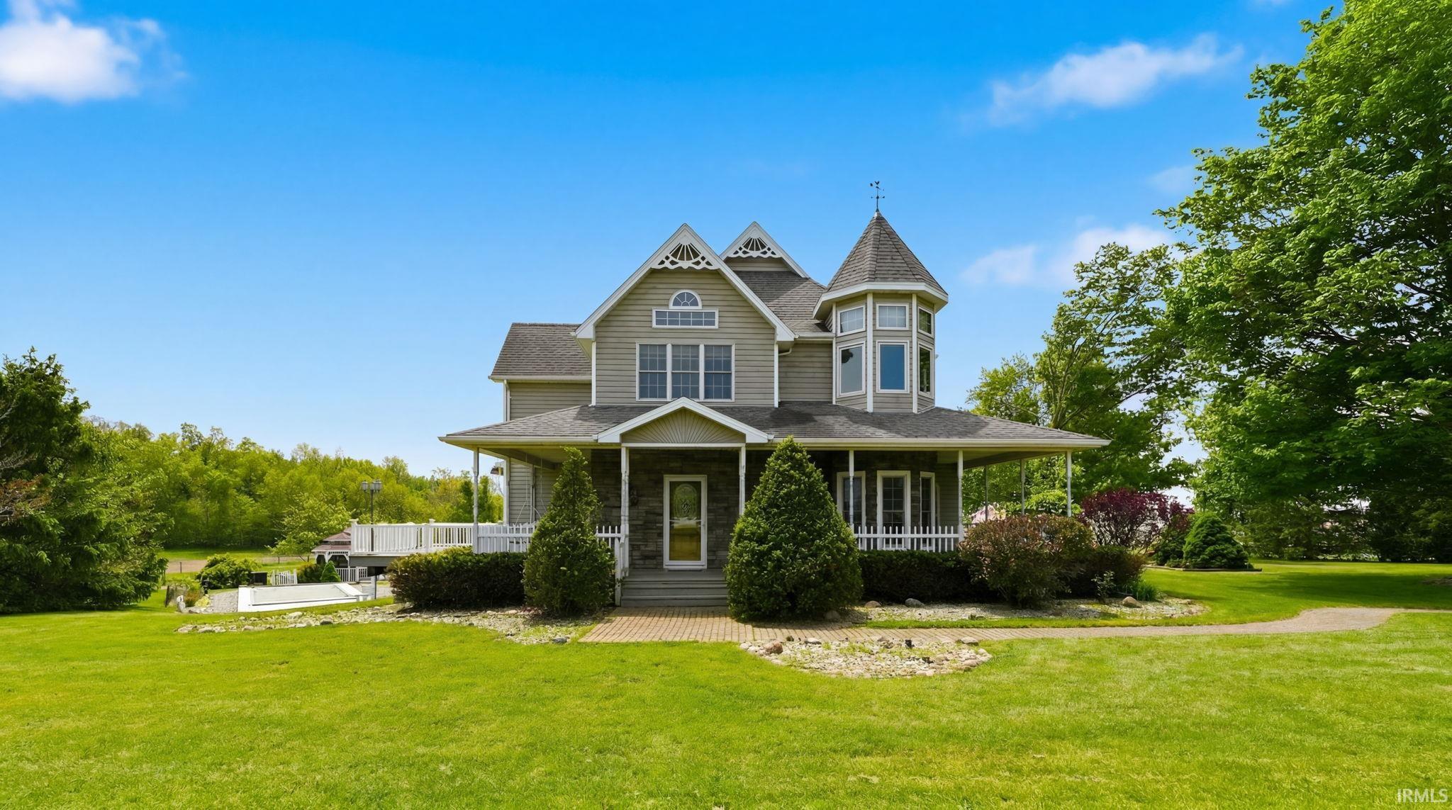 Grand Victorian-style residence featuring a stone facade entrance, extensive wrap-around porch with white railings, and a prominent turret
