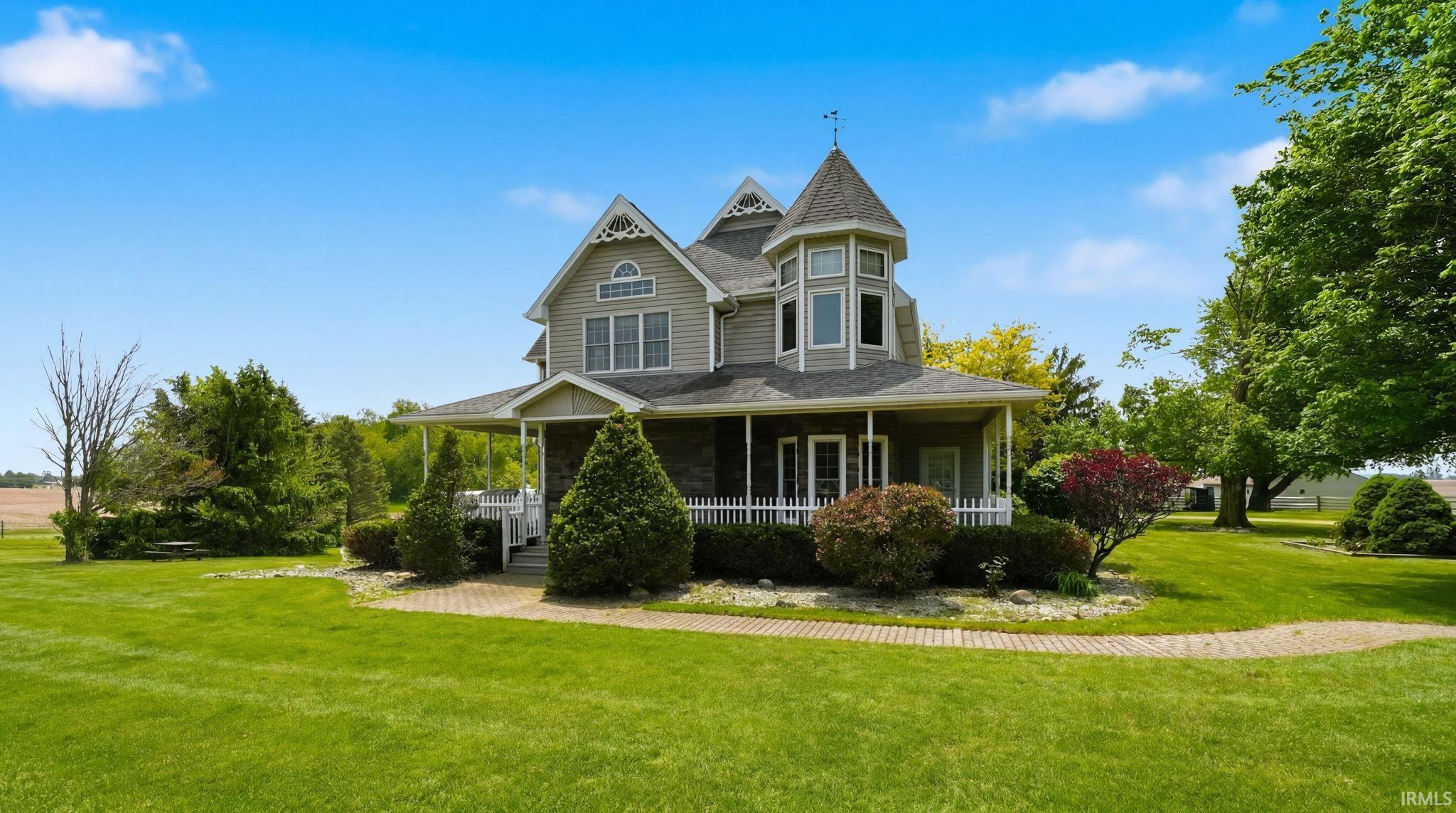 Victorian-inspired exterior featuring a prominent turret, wraparound porch with white railing, light gray siding, and stone accents