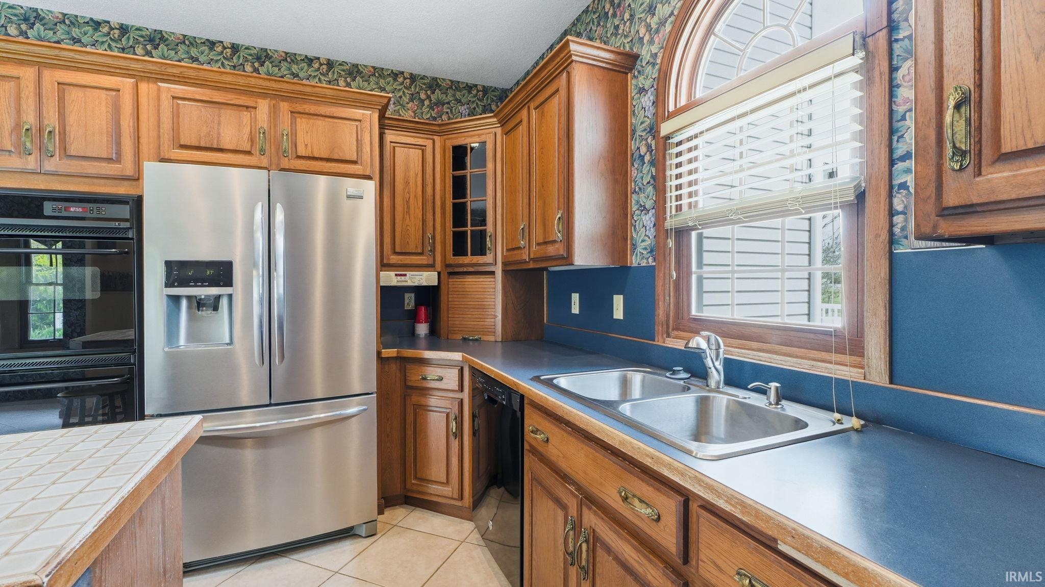 Kitchen featuring wood cabinetry, stainless steel appliances, a double basin sink, and a large arched window with blinds