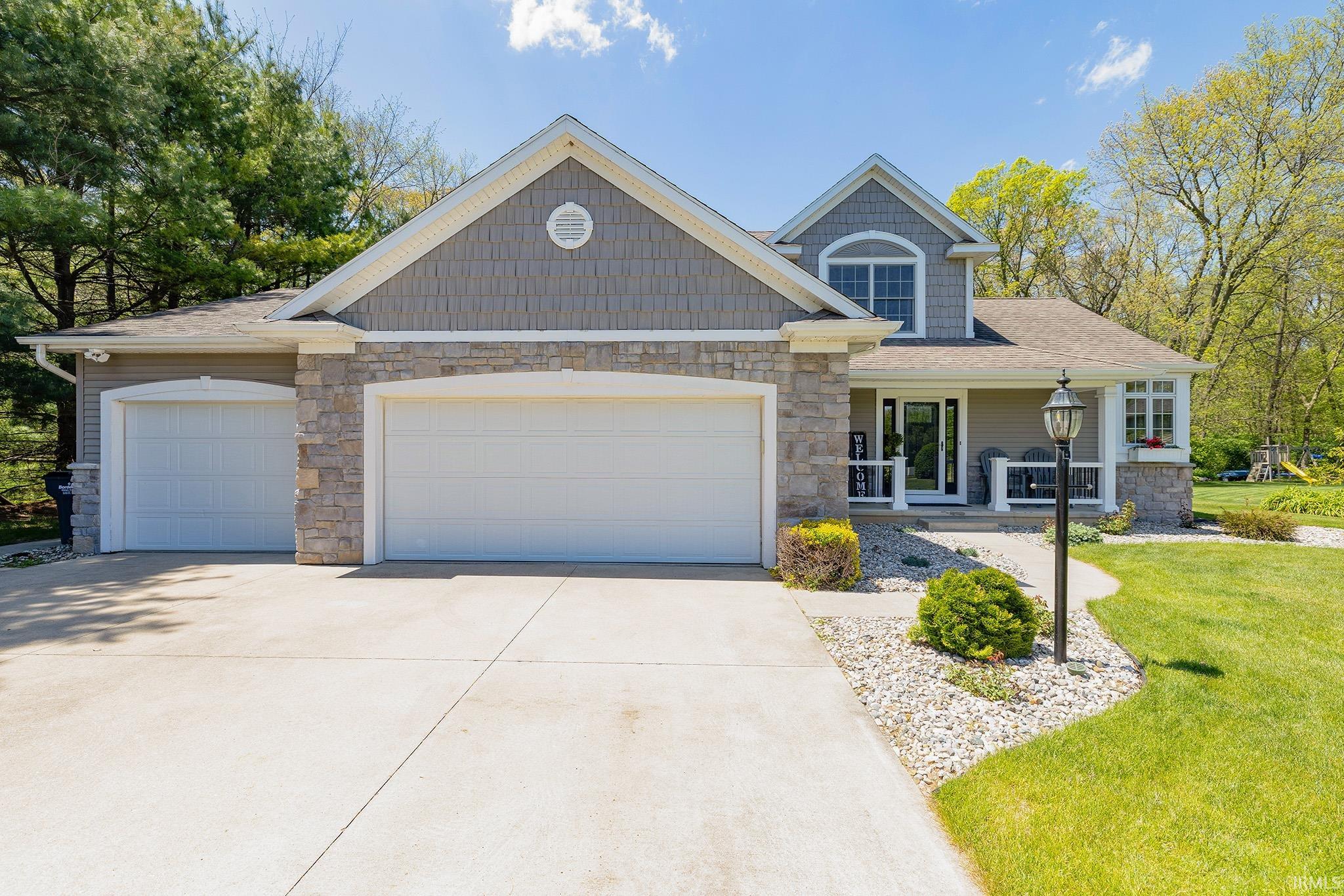 Stone and siding exterior featuring a three-car garage, covered porch, and arched second-story window