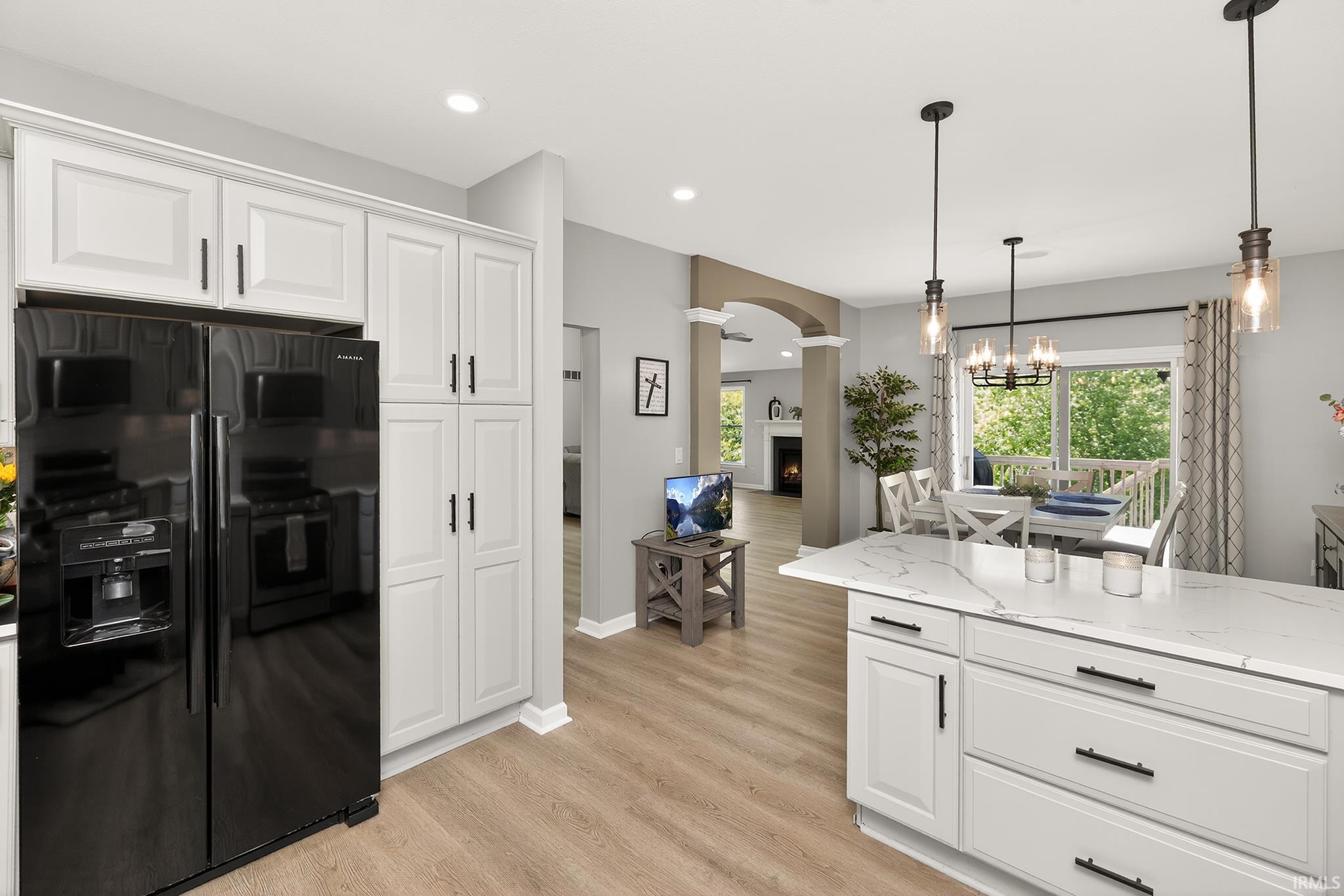 Kitchen featuring white shaker-style cabinetry, a black side-by-side refrigerator, a large center island with a light-toned countertop, and wood-finish flooring