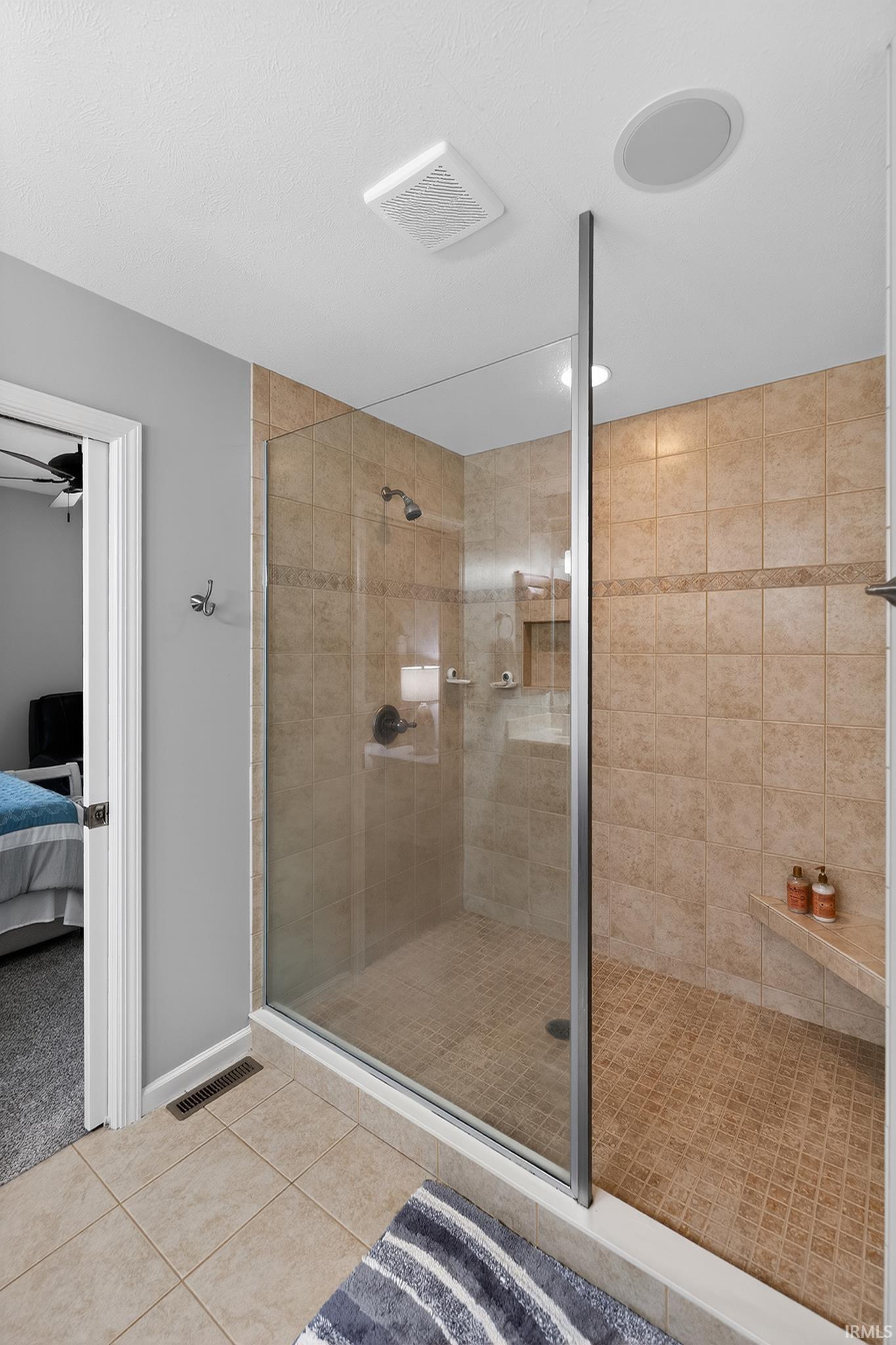 Walk-in shower featuring glass enclosure, tiled walls, built-in shelving, shower bench, and dark bronze fixtures