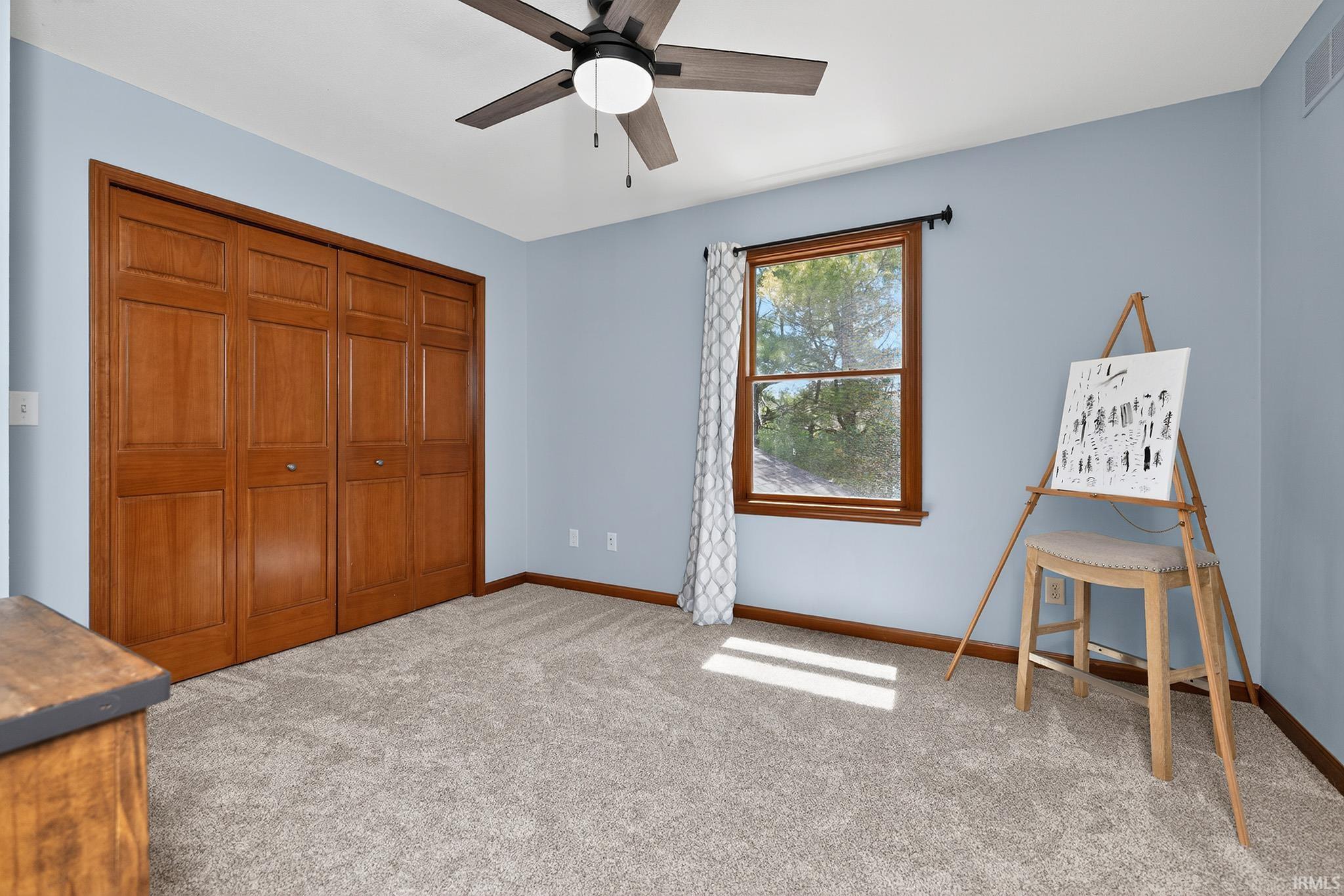 Textured gray carpeting, a ceiling fan with light fixture, and a window with wood trim