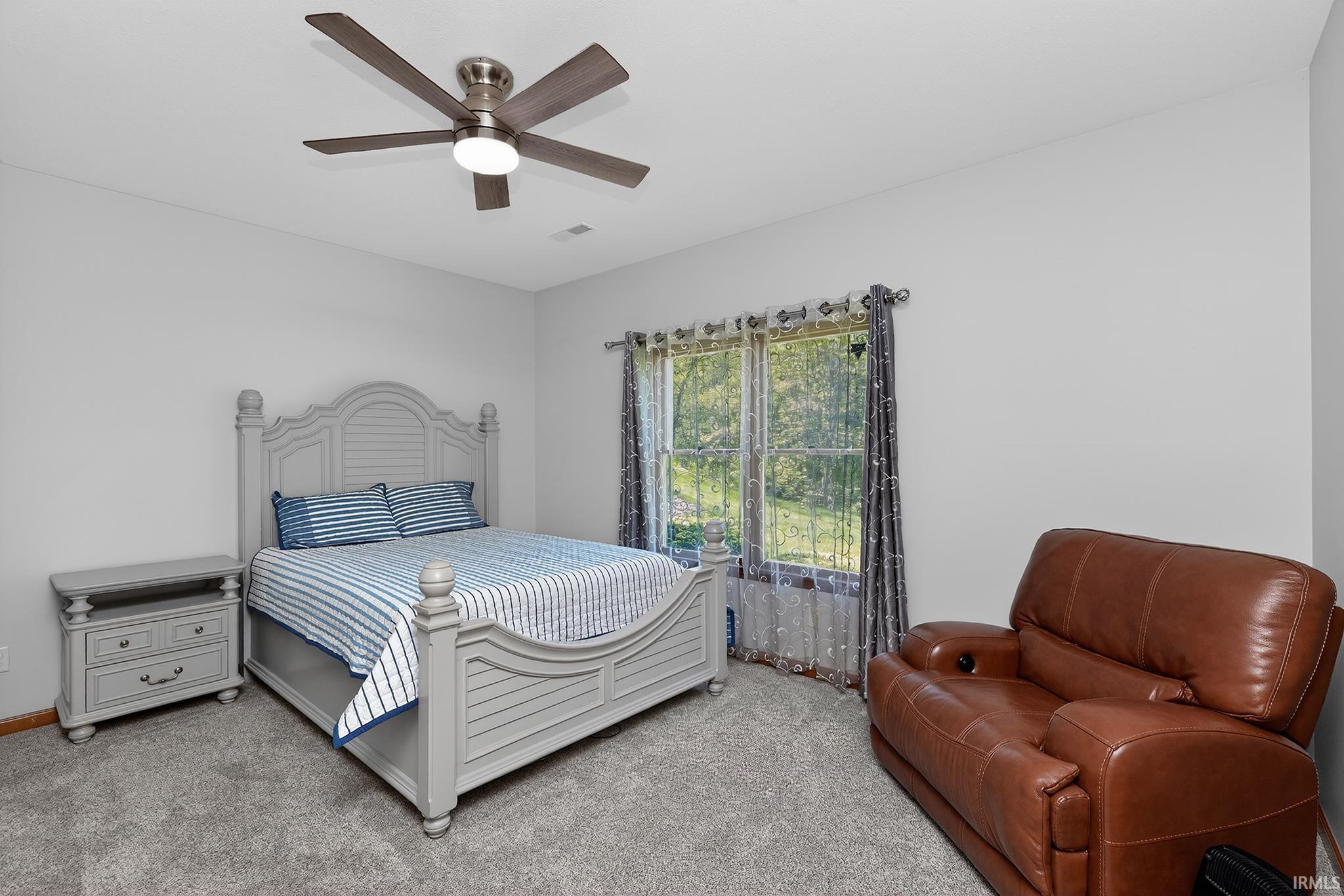 Carpeted room featuring a ceiling fan with light fixture, large window, and light gray wall paint