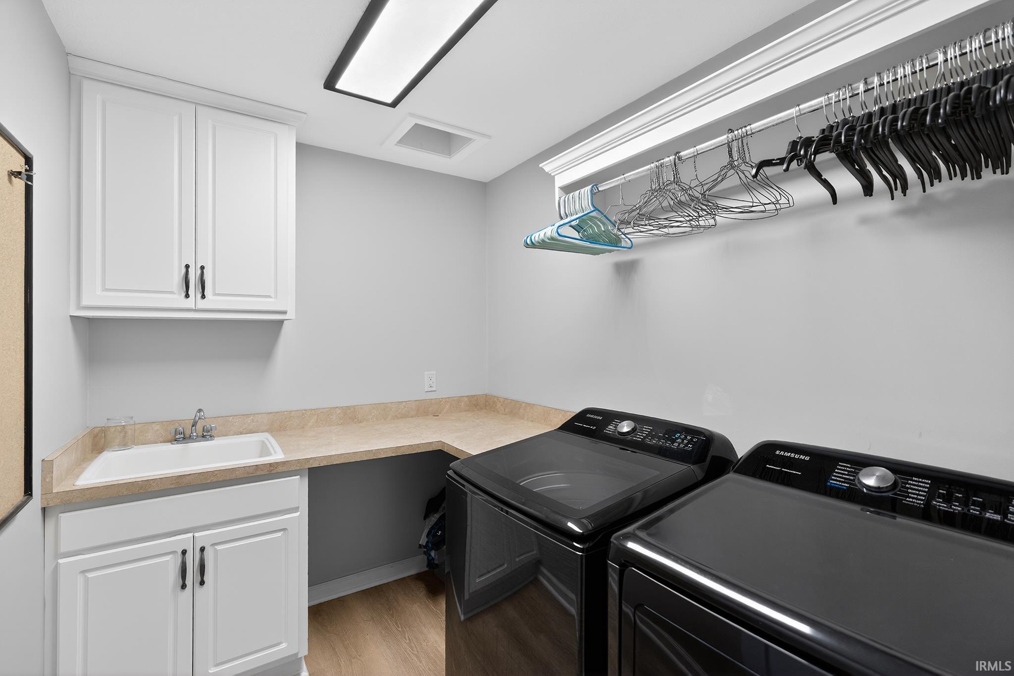 Laundry room with light wood-finish flooring, white cabinetry, and a utility sink