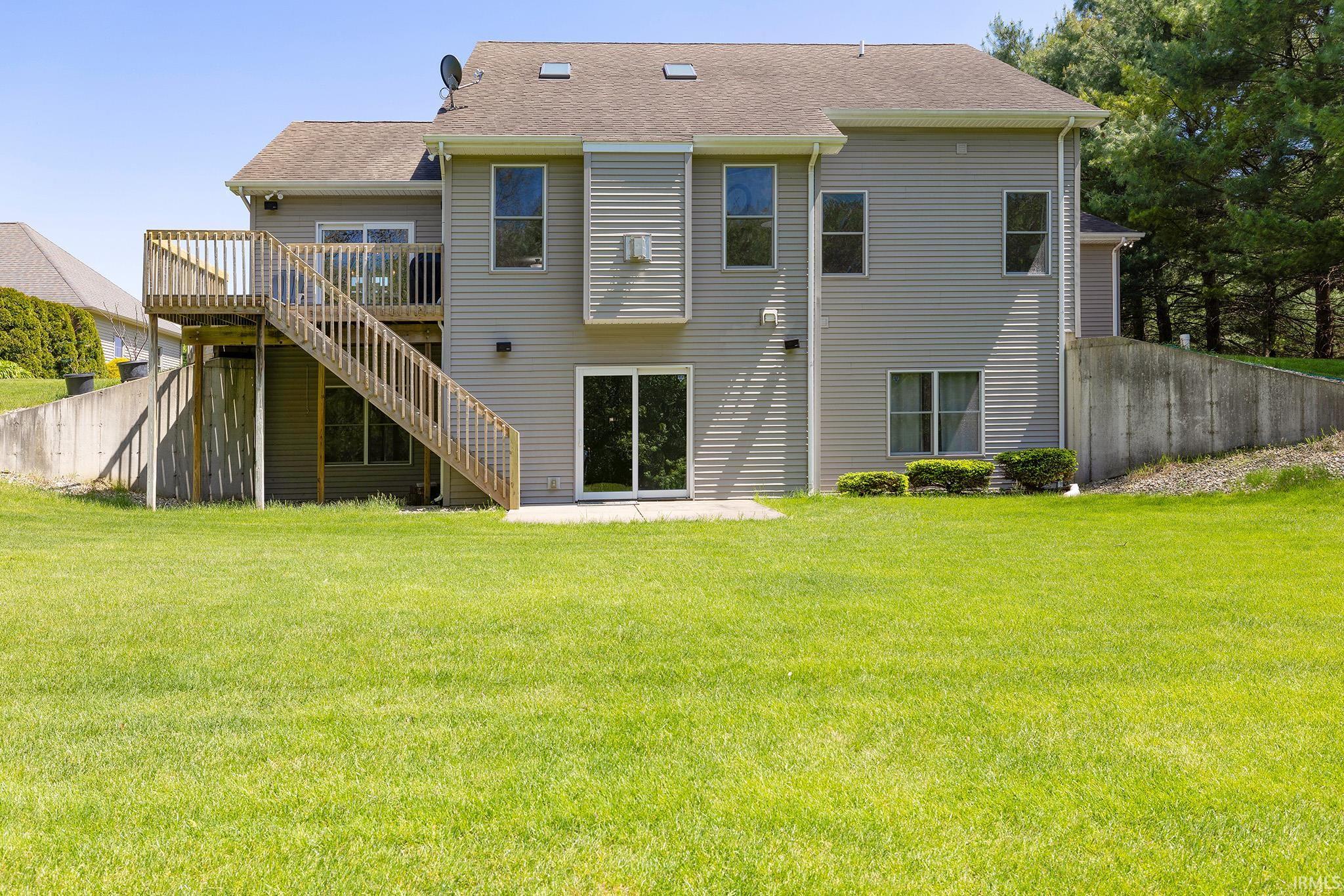 Rear exterior featuring a spacious wood deck with stairs, a concrete patio, and a sliding glass door