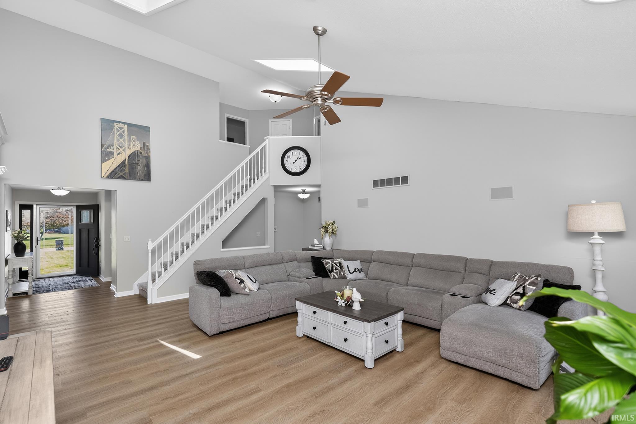 Spacious living area featuring wood-finish flooring, vaulted ceilings, skylights, and a ceiling fan