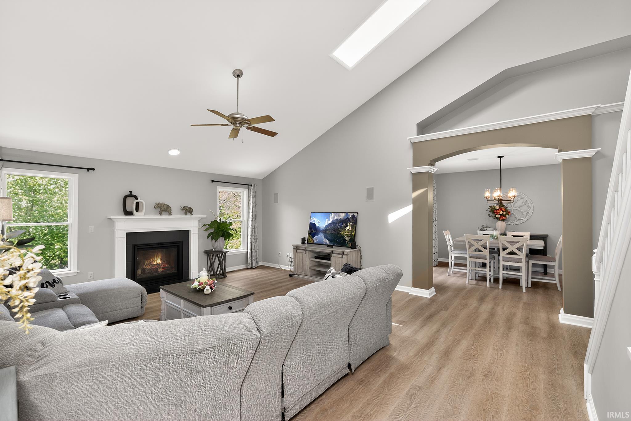 Living area featuring a vaulted ceiling with skylight, wood-finish flooring, a fireplace with a white mantel, and an arched entry to a distinct dining area