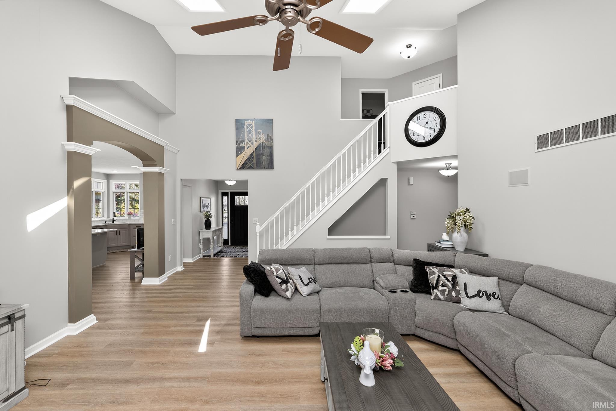 Vaulted living room featuring light wood-finish flooring, a contemporary ceiling fan, and skylights