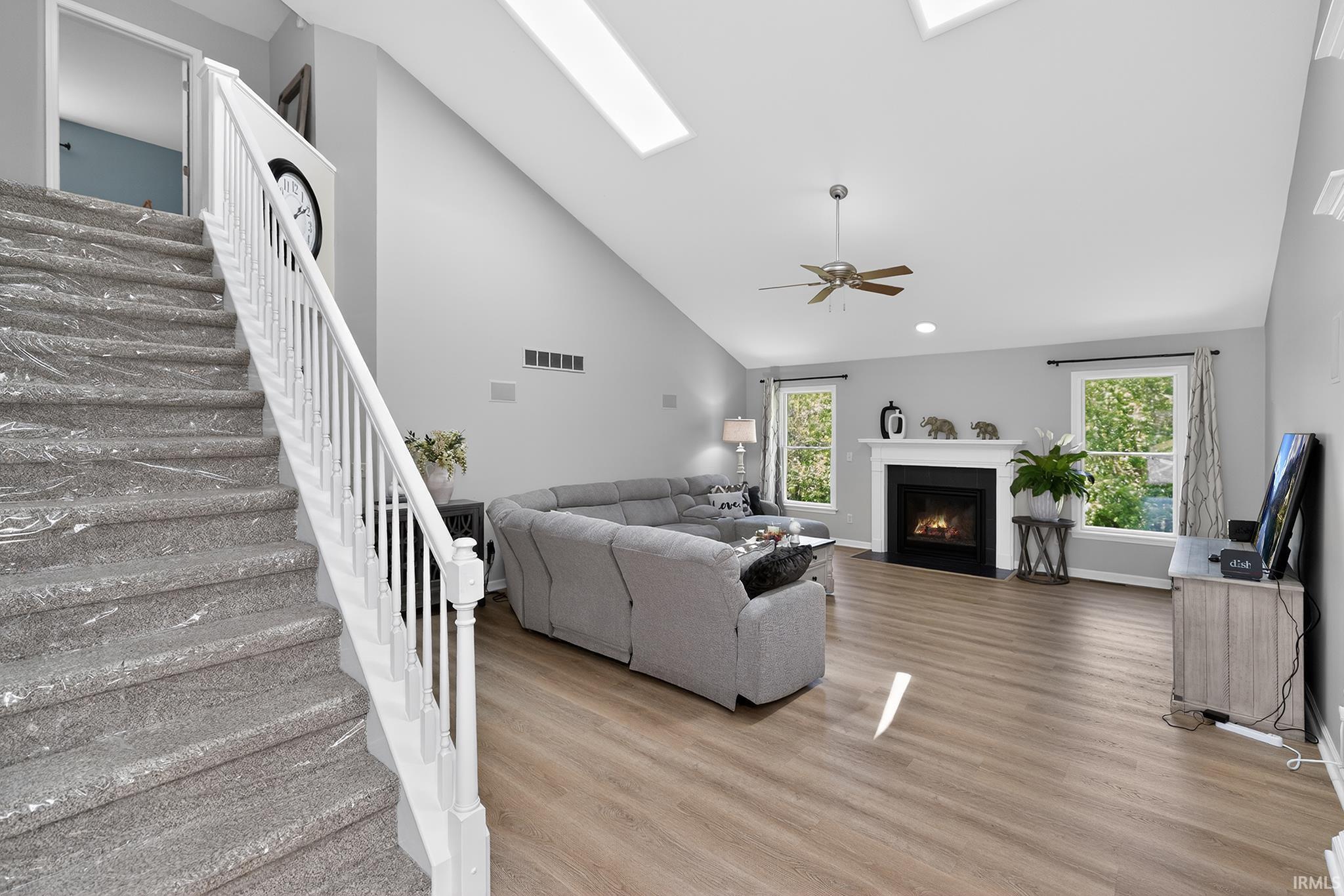 Living area featuring vaulted ceilings with skylights, wood-finish flooring, and a fireplace with a white mantel