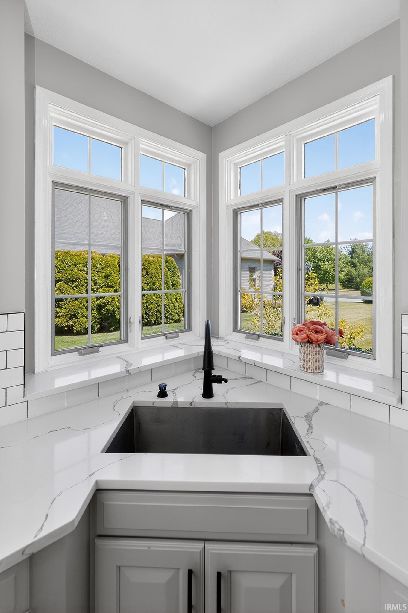 Corner window configuration with multiple casement windows, a deep single-basin sink, matte black faucet, light grey cabinetry, and white countertops with subtle veining