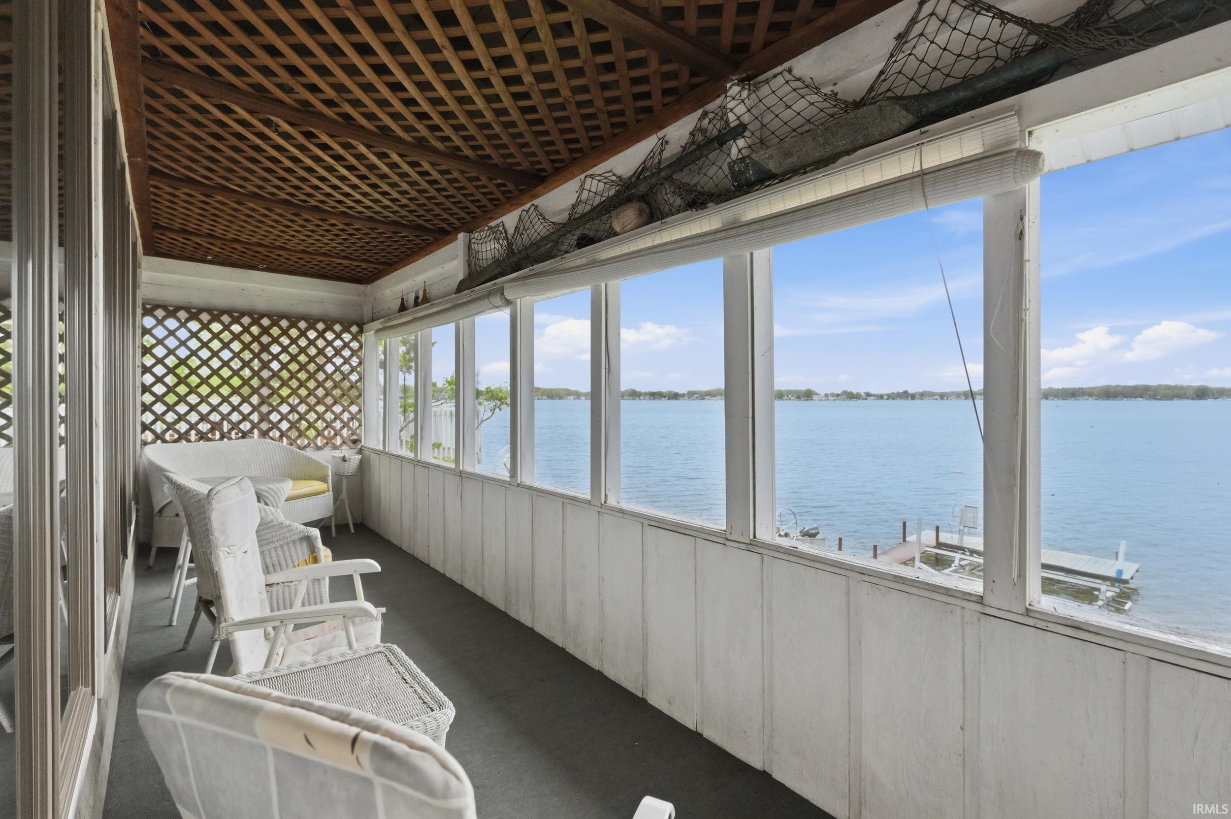 Enclosed porch featuring multiple windows overlooking a body of water, a lattice privacy screen, and a wood lattice ceiling
