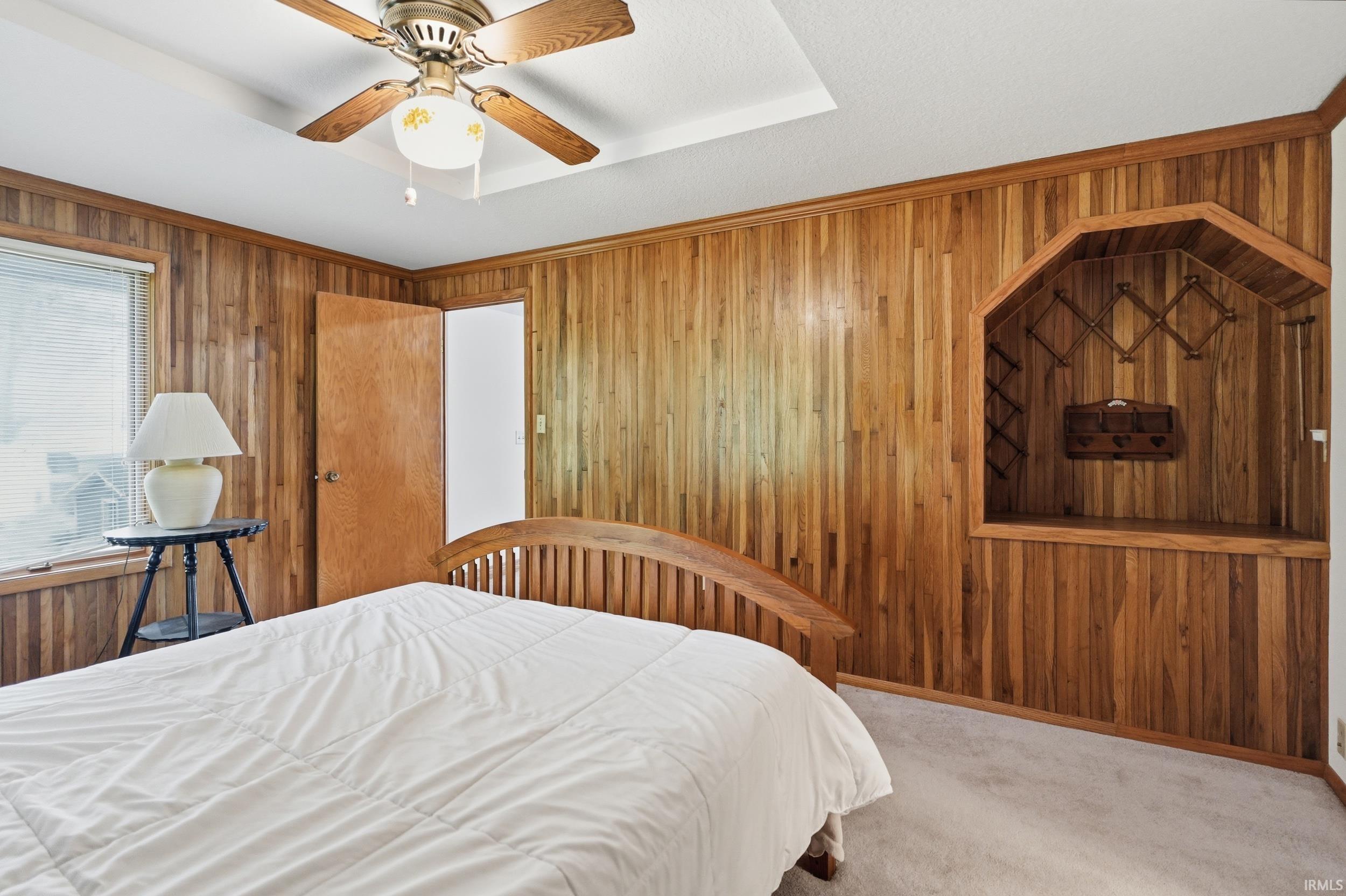 Wood-paneled room featuring a tray ceiling with a ceiling fan, a built-in recessed niche with shelving, and light-colored carpeting