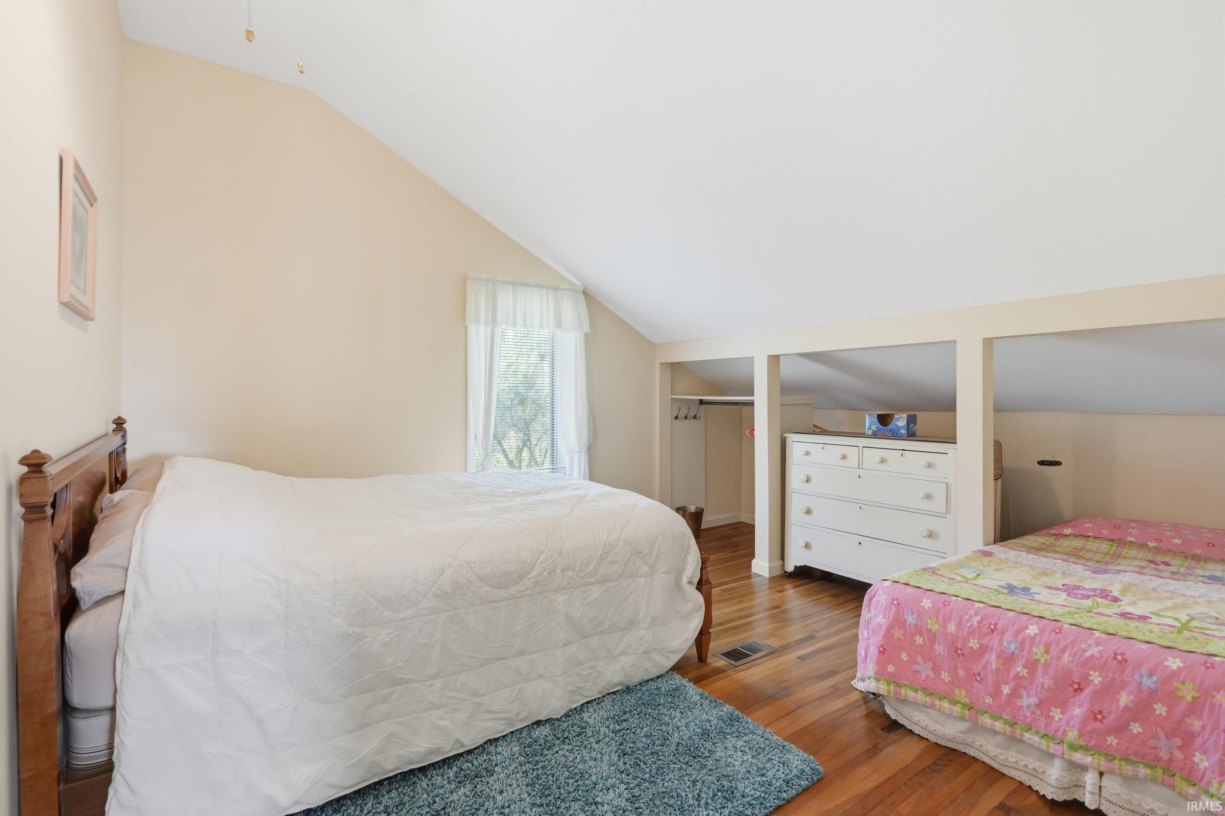 Room featuring vaulted ceilings, wood-finish flooring, and a window with natural light