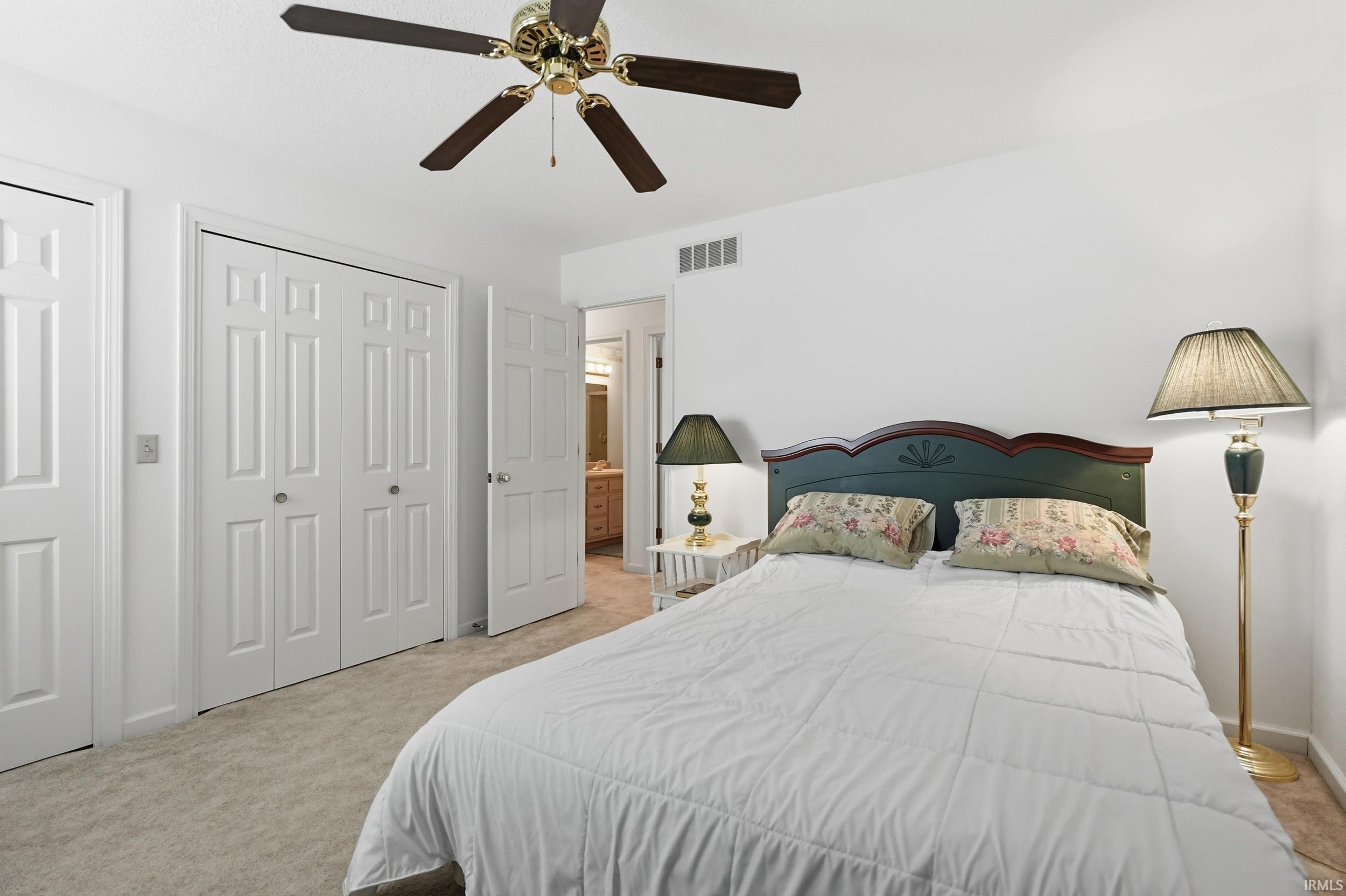 Carpeted room featuring a ceiling fan with dark wood-finish blades, two panel doors, and bifold closet doors