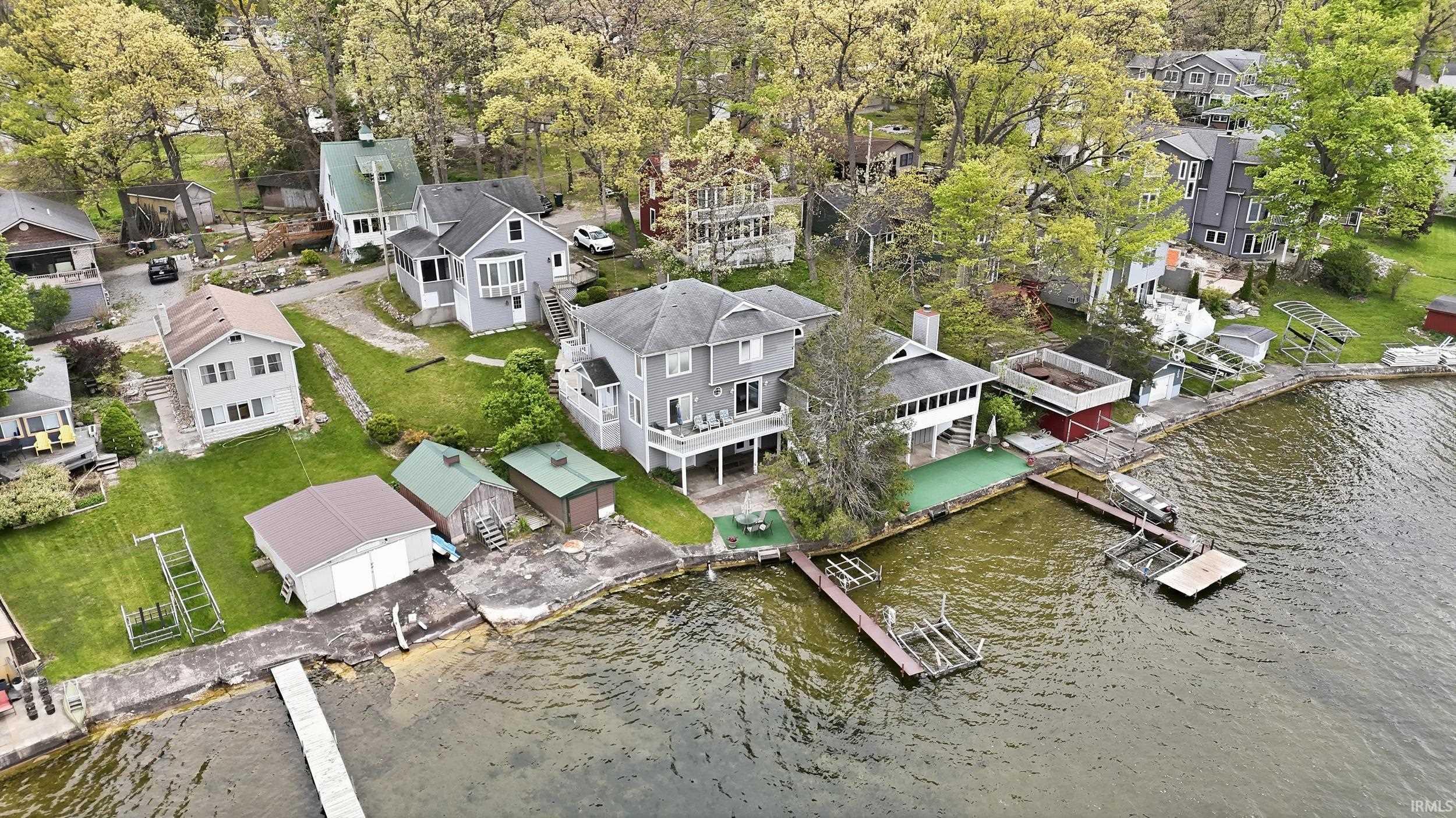 Waterfront property featuring a multi-story residence with a rear deck, multiple boat docks, a boathouse, and additional storage sheds