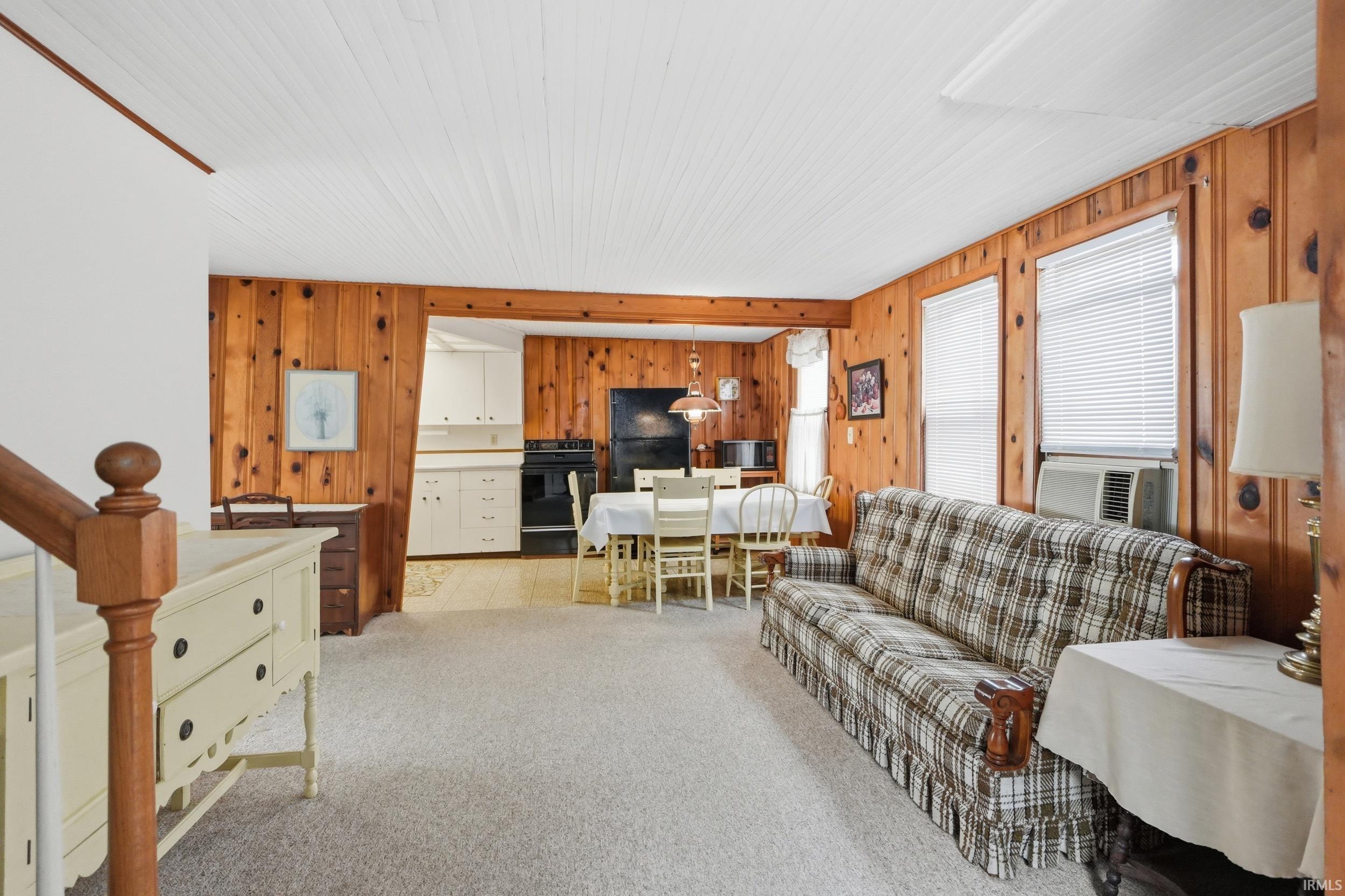 Open-concept interior featuring wood paneling, white beadboard ceiling, and light-toned carpet flooring