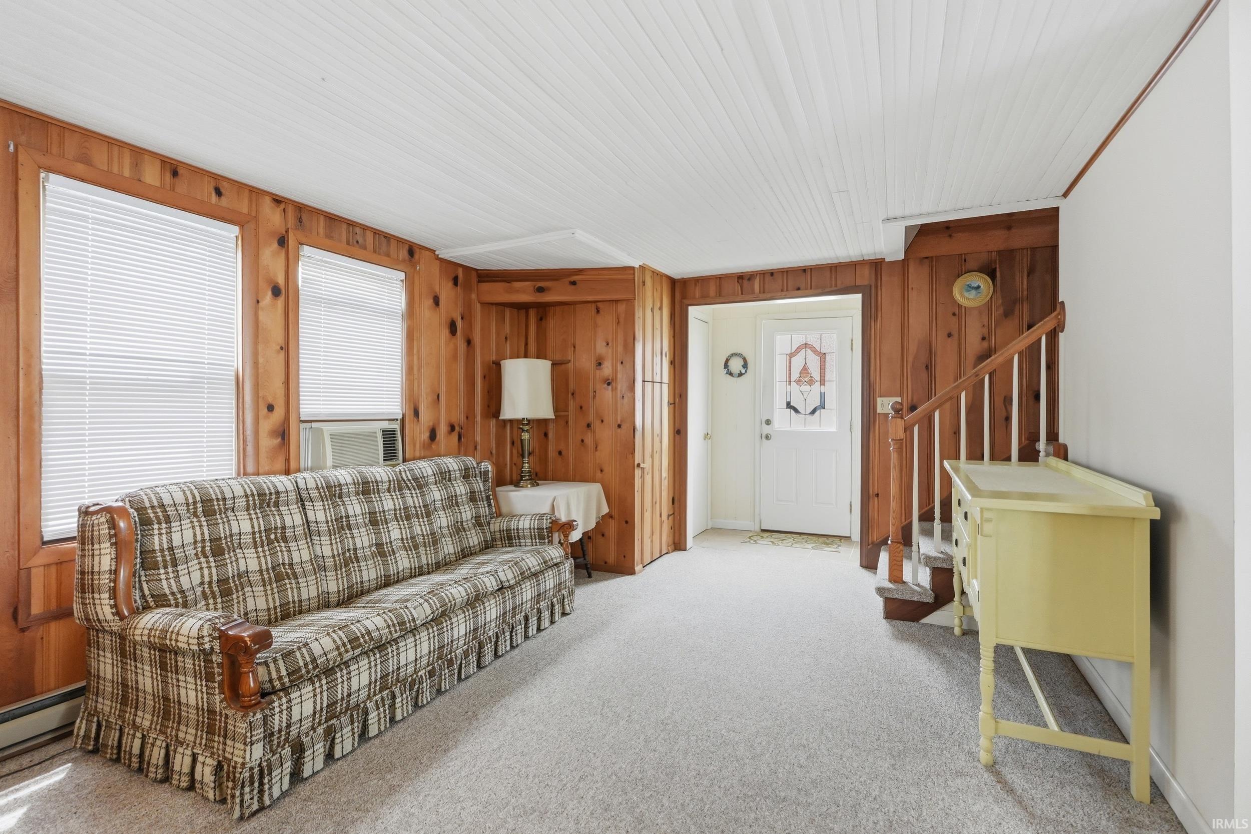 Carpeted living space featuring wood paneling, white paneled ceiling, and a white entry door with decorative glass