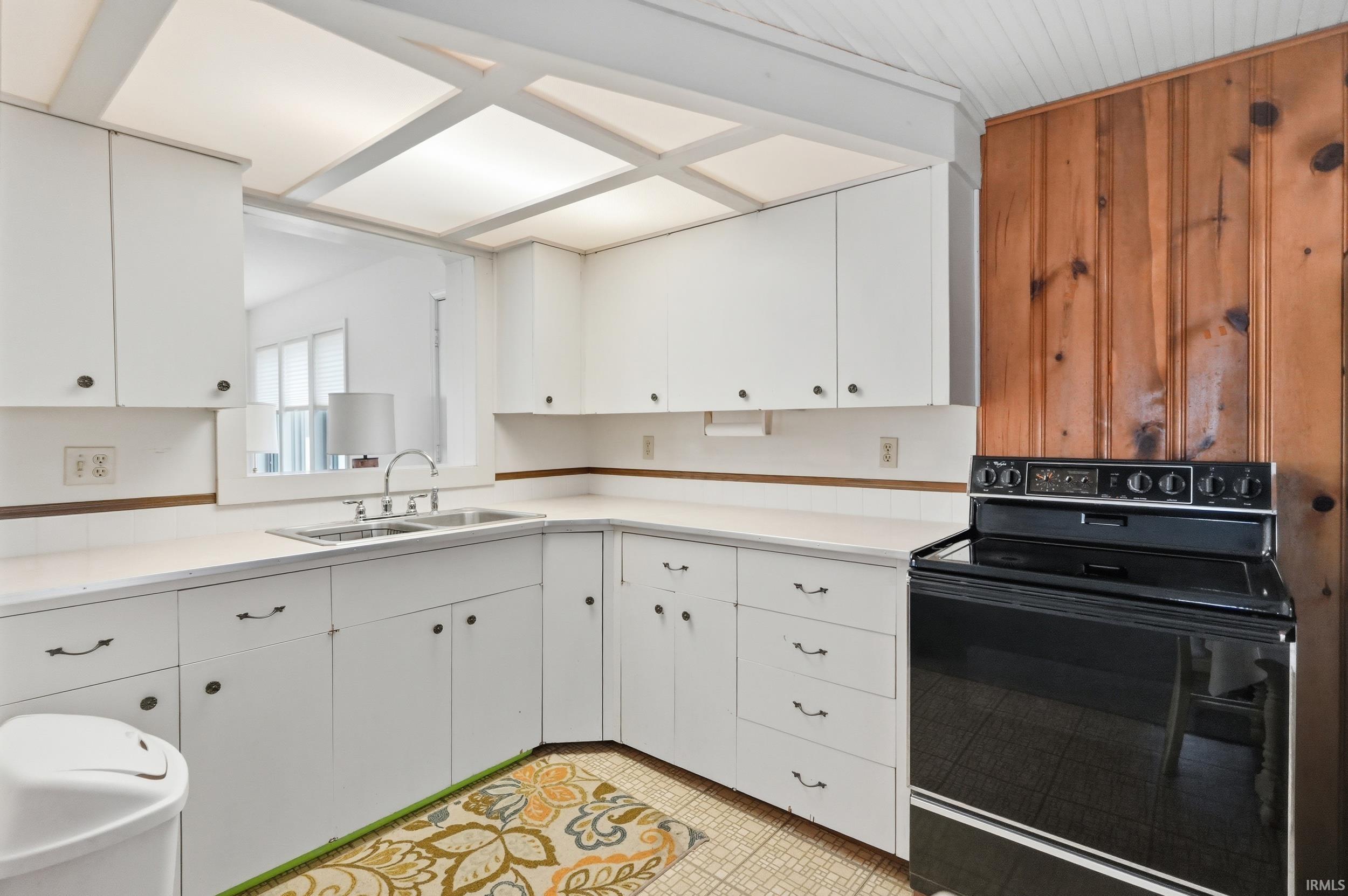 Kitchen featuring white cabinetry, a double basin stainless steel sink, black range, wood paneling, and a white beadboard ceiling