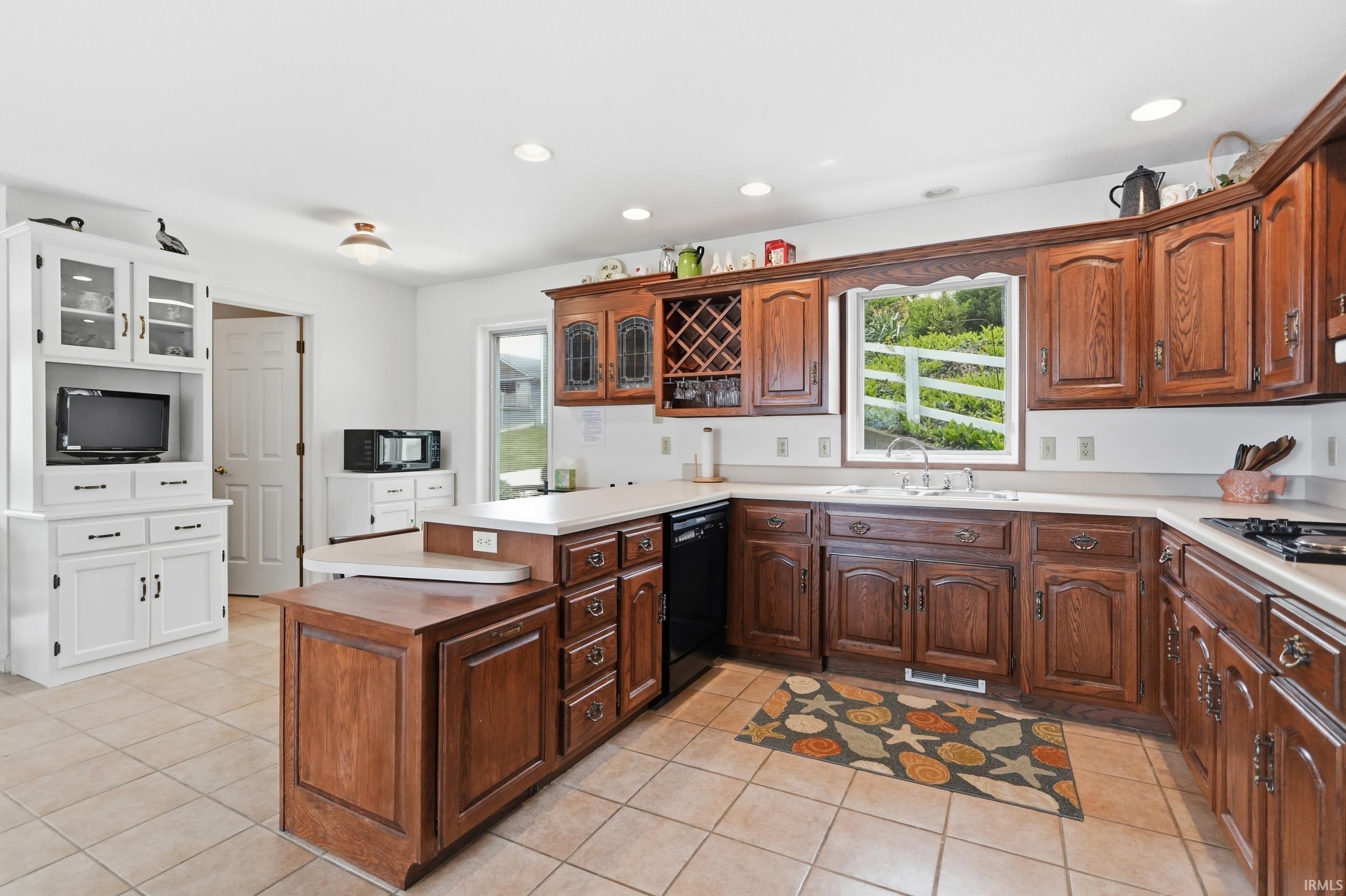 Spacious kitchen with tile flooring, wood cabinetry, built-in wine rack, and a white hutch with glass-front upper cabinets