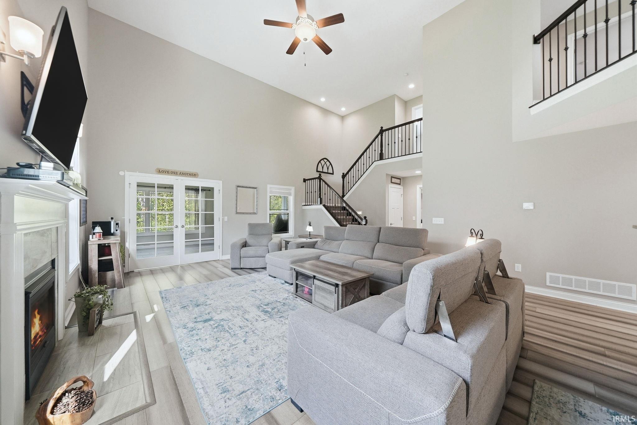 Two-story living area with high ceilings, wood-finish flooring, and a fireplace with a white mantel