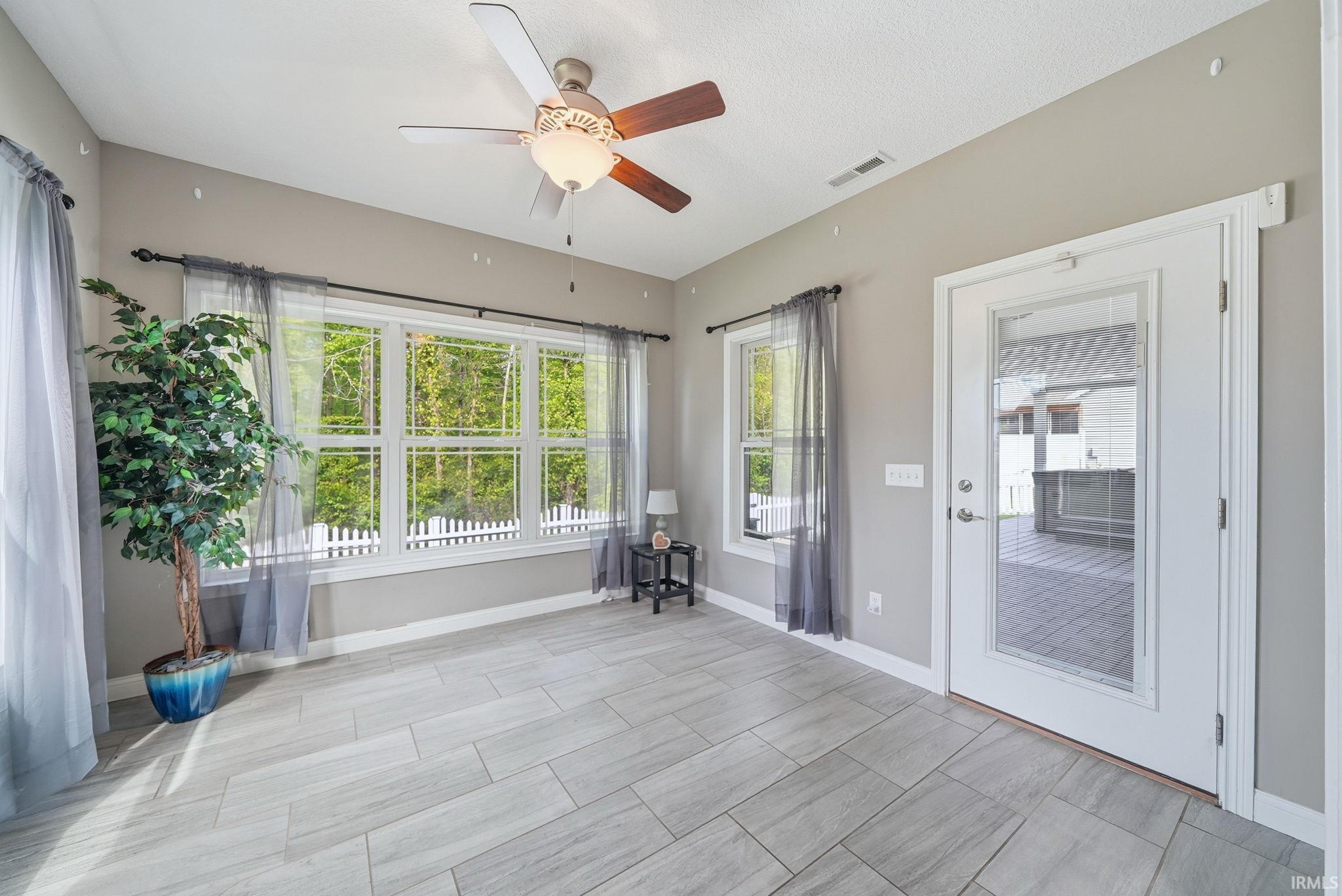 Sunroom featuring large windows, light gray tile flooring, a ceiling fan, and direct access to an outdoor patio area