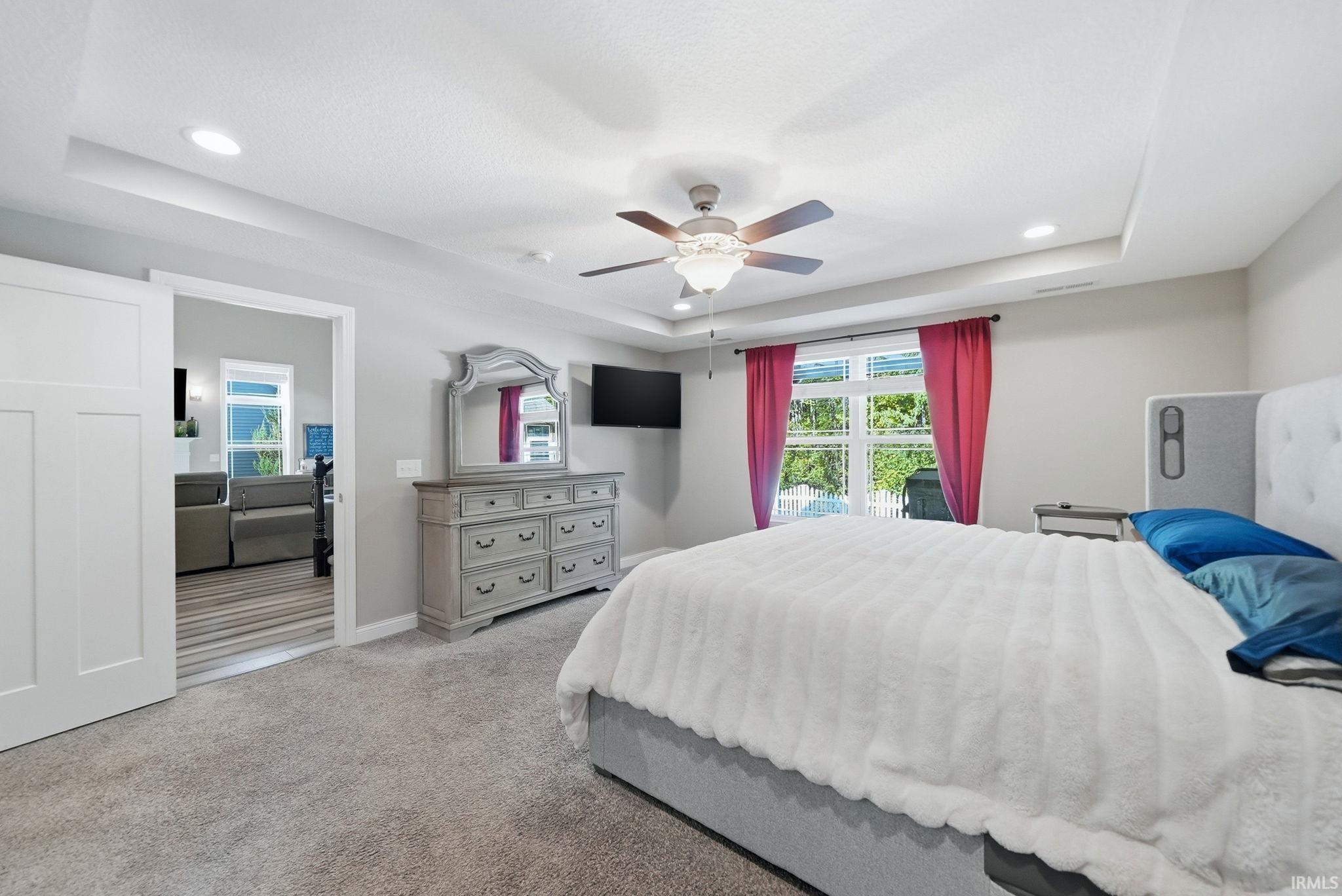 Carpeted bedroom featuring a tray ceiling with recessed lighting and a ceiling fan