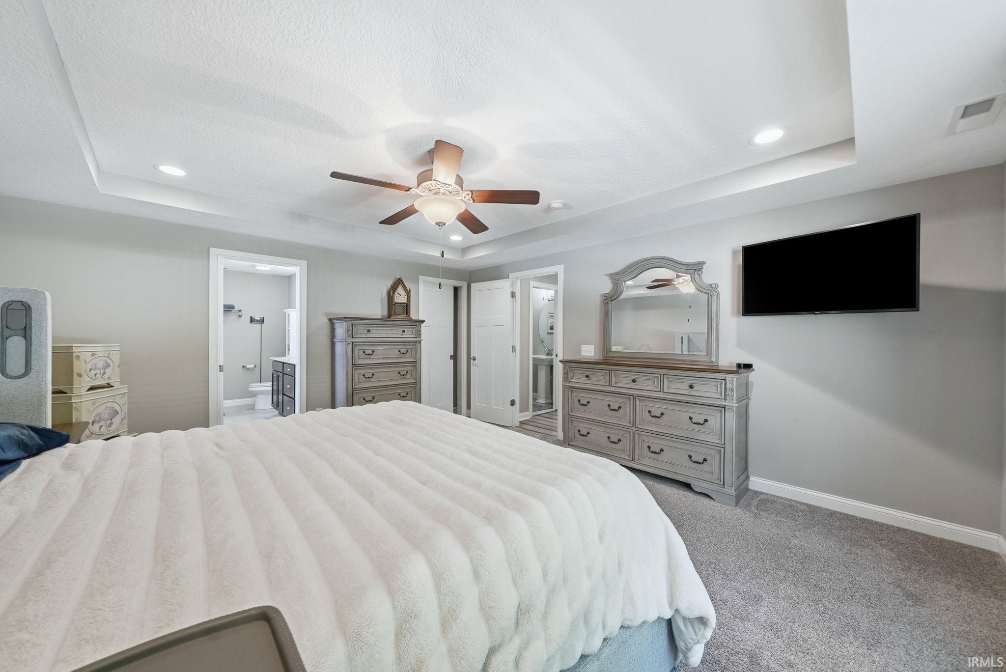 Carpeted bedroom featuring a tray ceiling with recessed lighting and a ceiling fan, light gray wall paint, and white trim