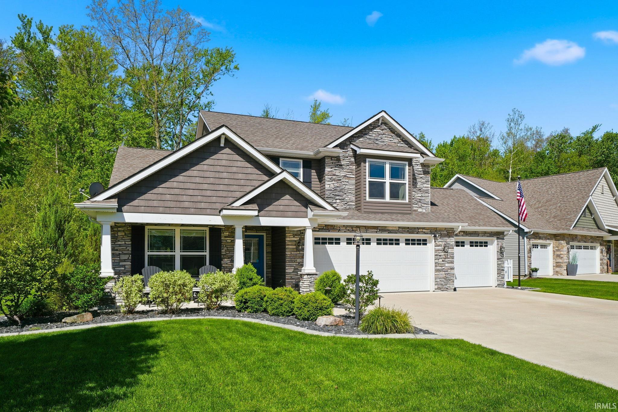 Stone and shake-sided exterior featuring multiple gables, a covered front porch, and an attached three-car garage