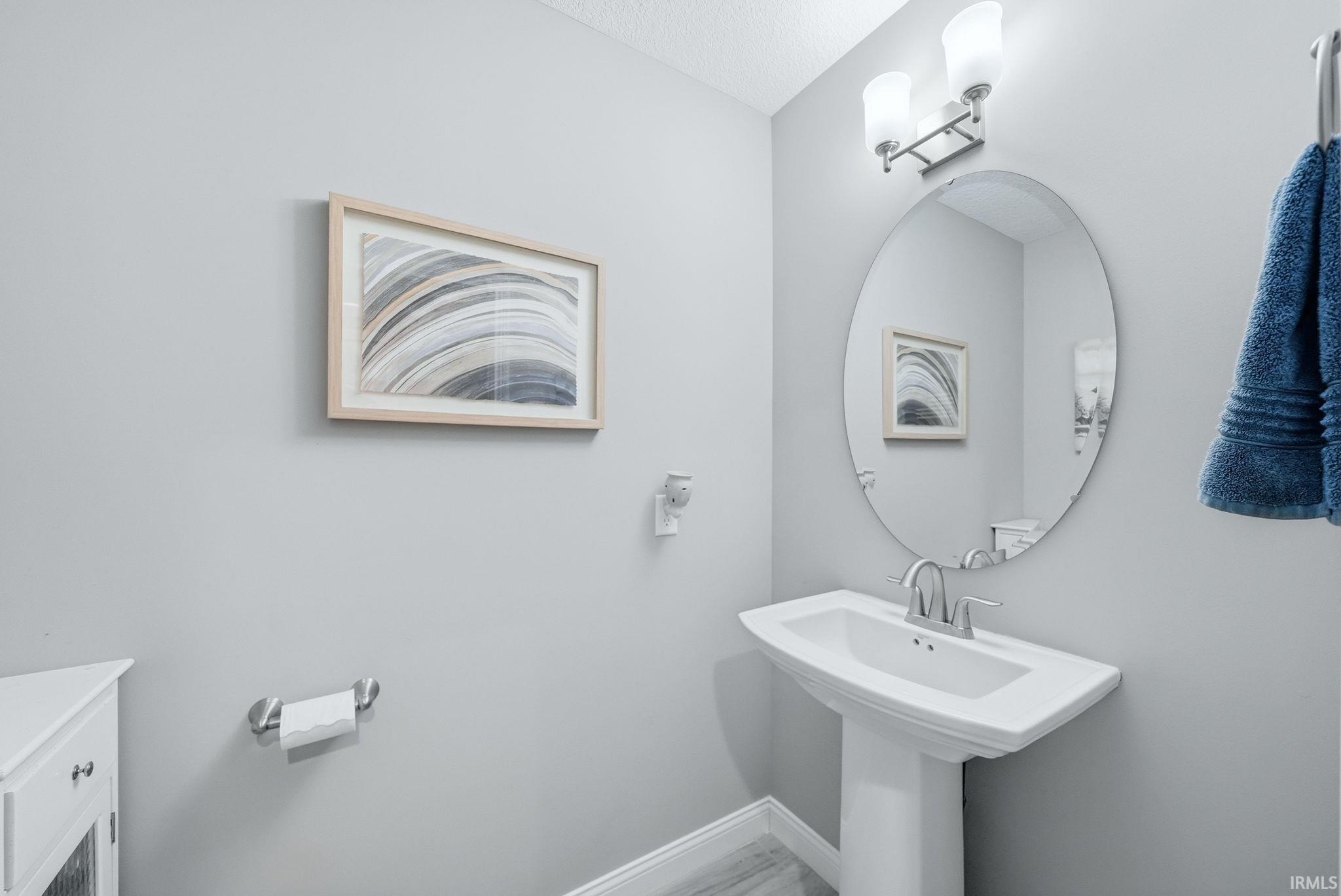 Pedestal sink with chrome faucet, an oval frameless mirror, and a two-light vanity fixture